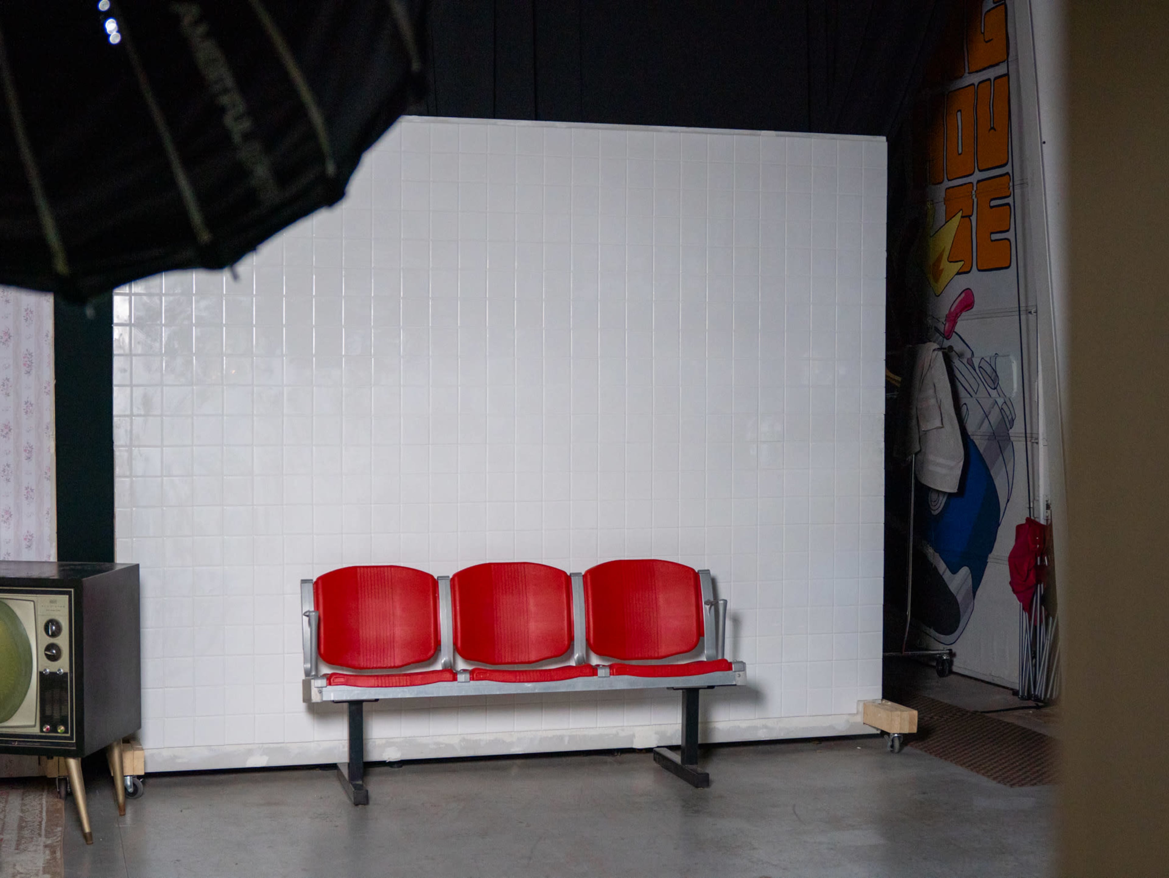 A row of three red chairs is positioned in front of a large white tile backdrop.