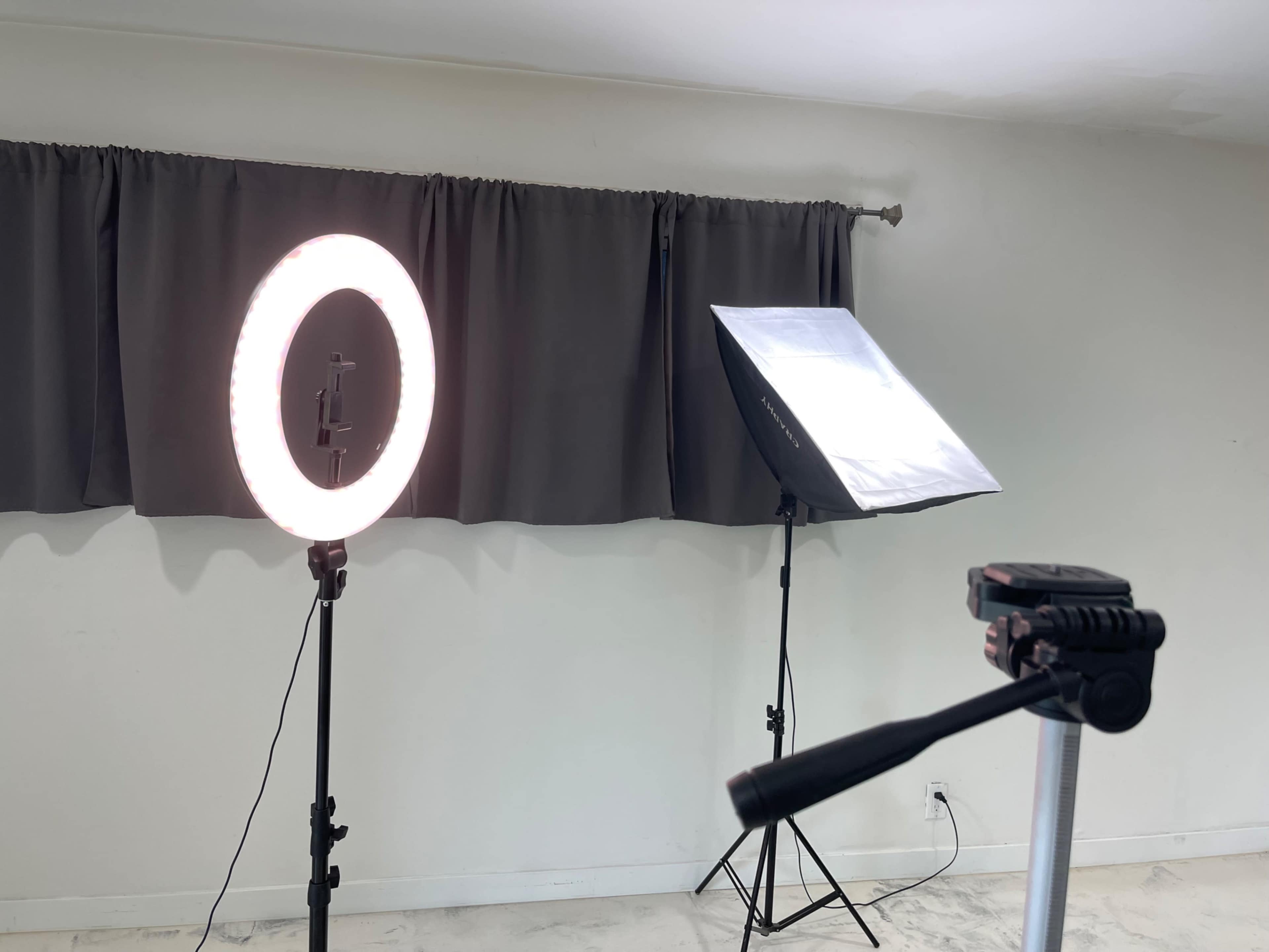 A photography setup with a ring light and a softbox positioned near a curtain.