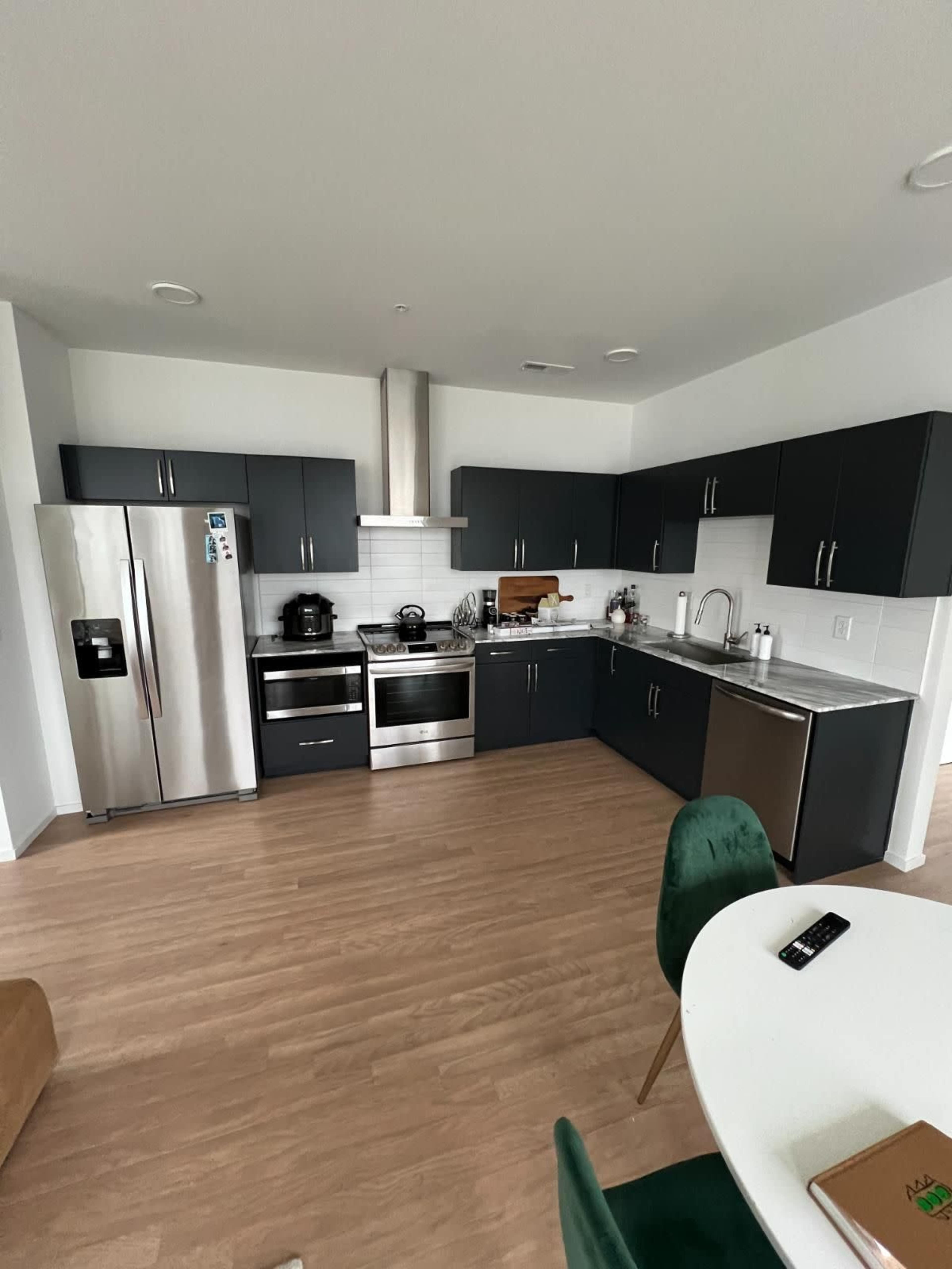 A modern kitchen with dark cabinetry, stainless steel appliances, and wooden flooring.