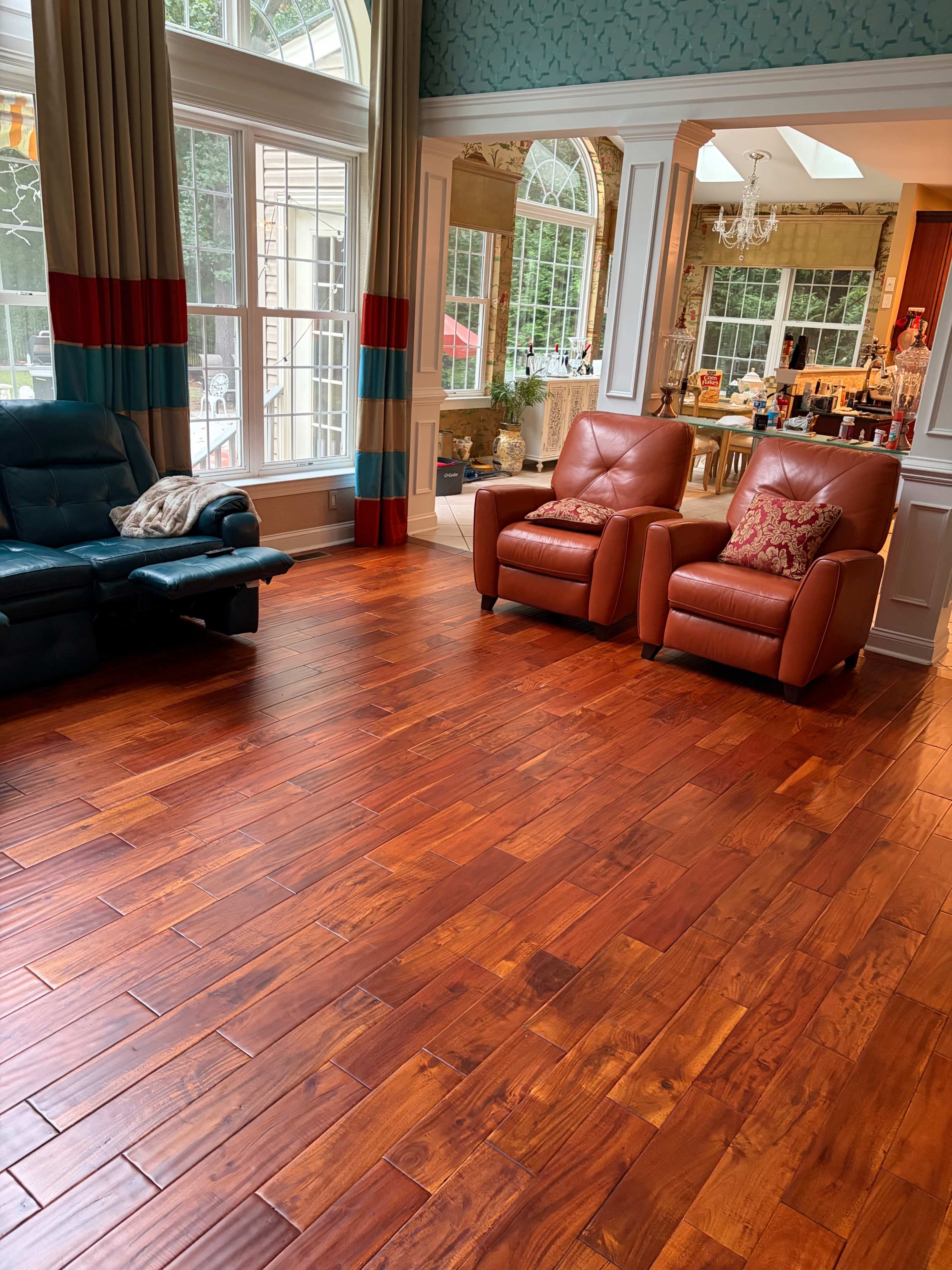 The image shows a spacious living area with hardwood flooring, featuring two leather armchairs and large windows that allow natural light to enter.