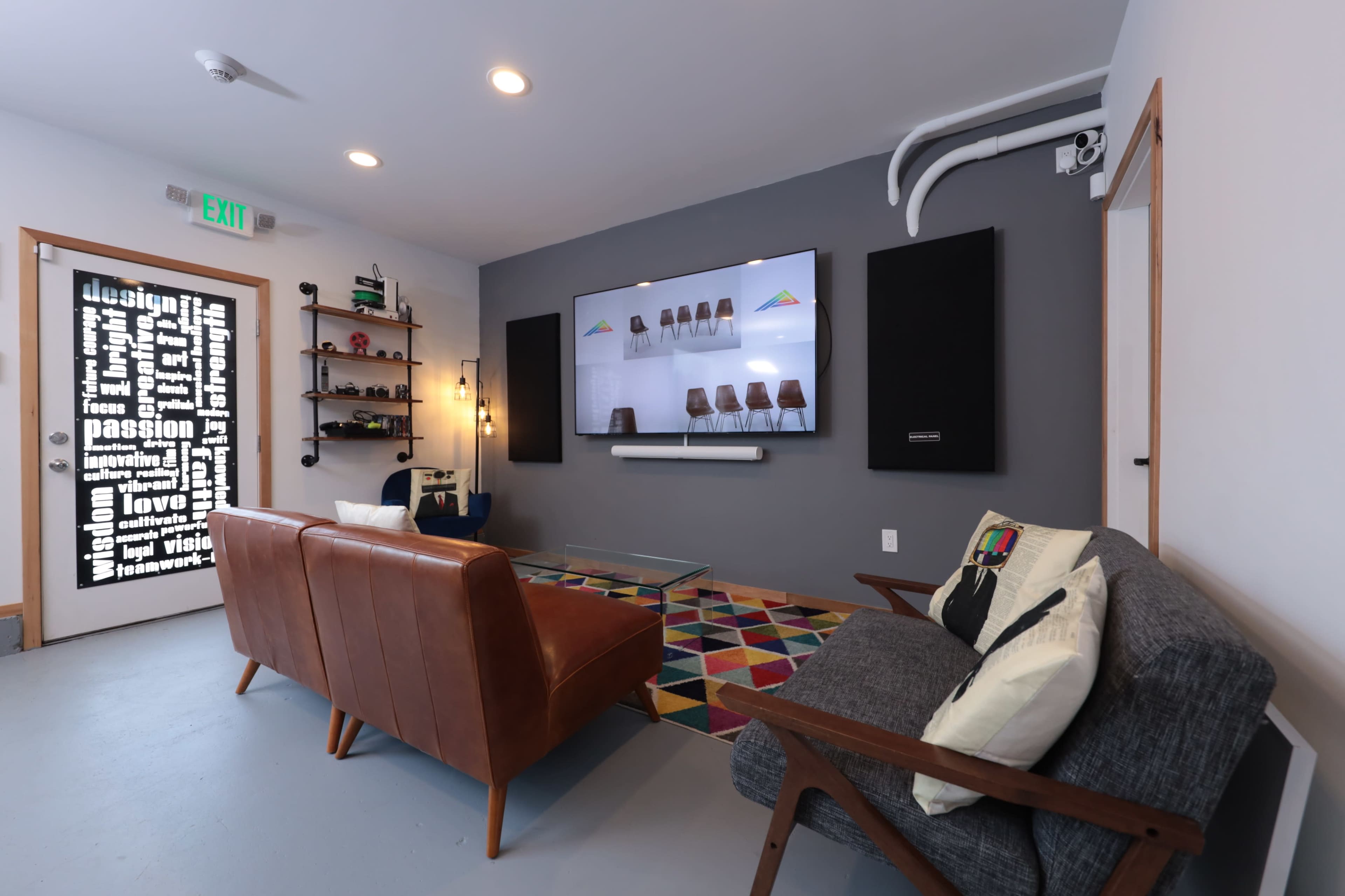 The image shows a modern living room with a television mounted on the wall, two sofas, and a colorful patterned rug.