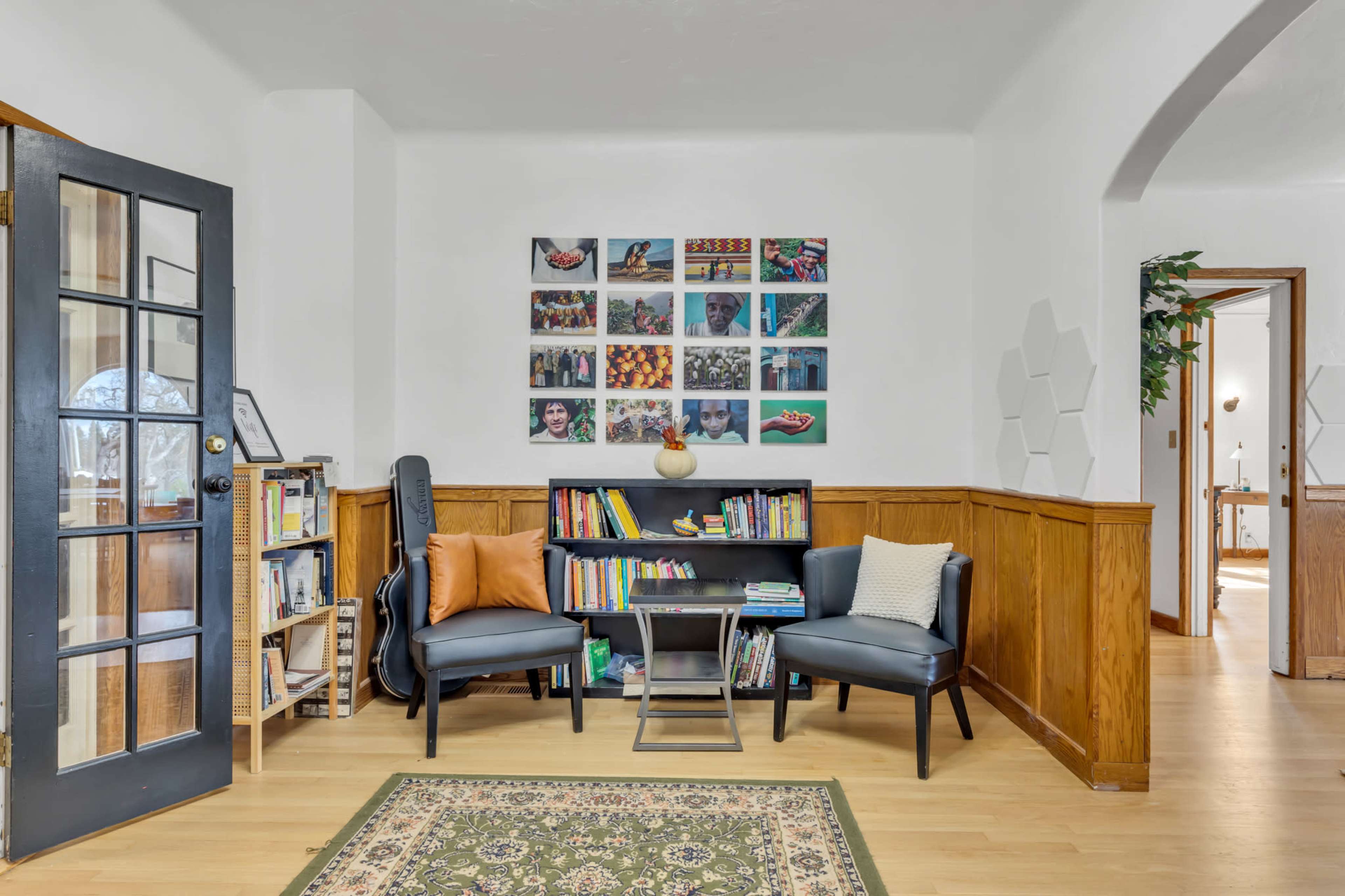 A cozy reading corner features two chairs, a small bookshelf filled with books, and a colorful wall display of photographs.