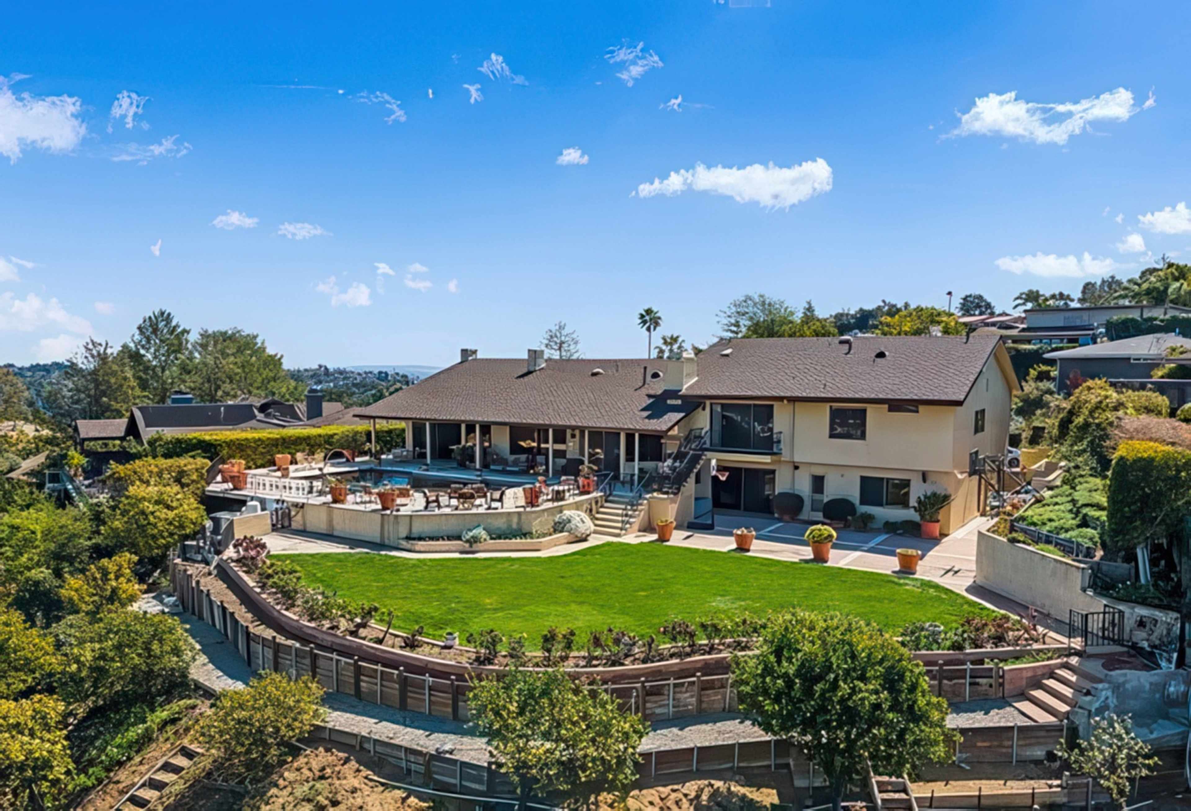 A hillside home features a large backyard with a swimming pool, surrounded by landscaped greenery and outdoor seating areas.