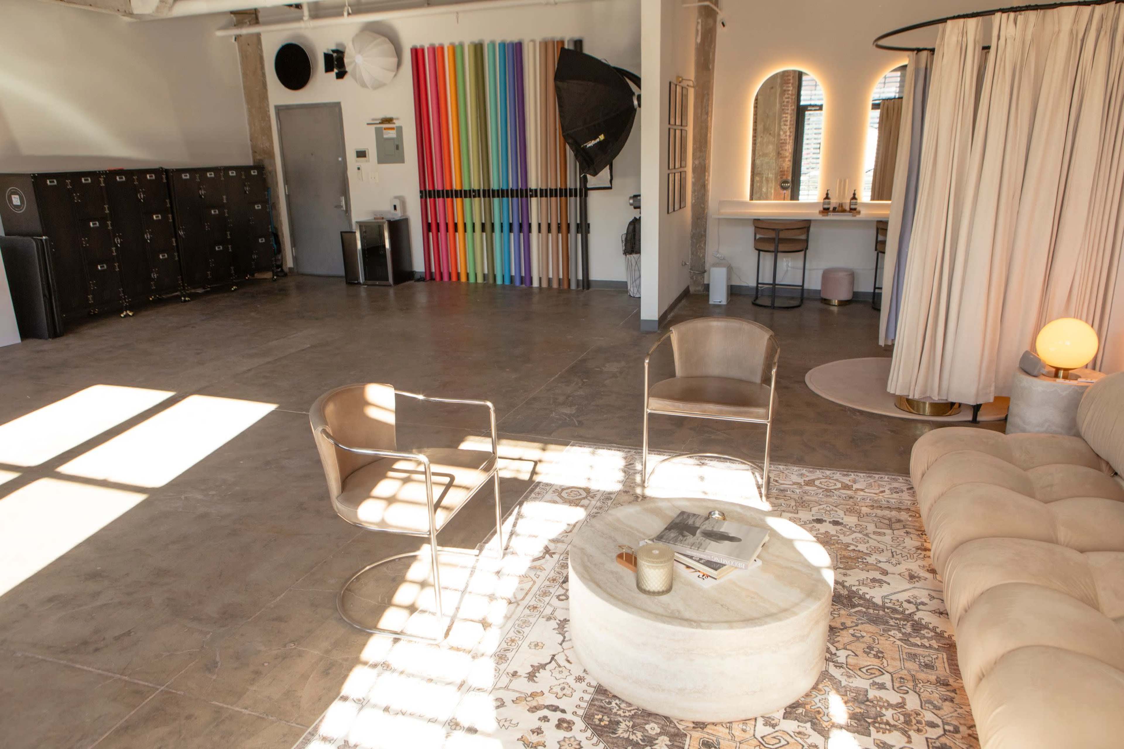 The image shows a spacious interior with a seating area featuring two chairs and a round coffee table, along with colorful vertical panels and lockers in the background.