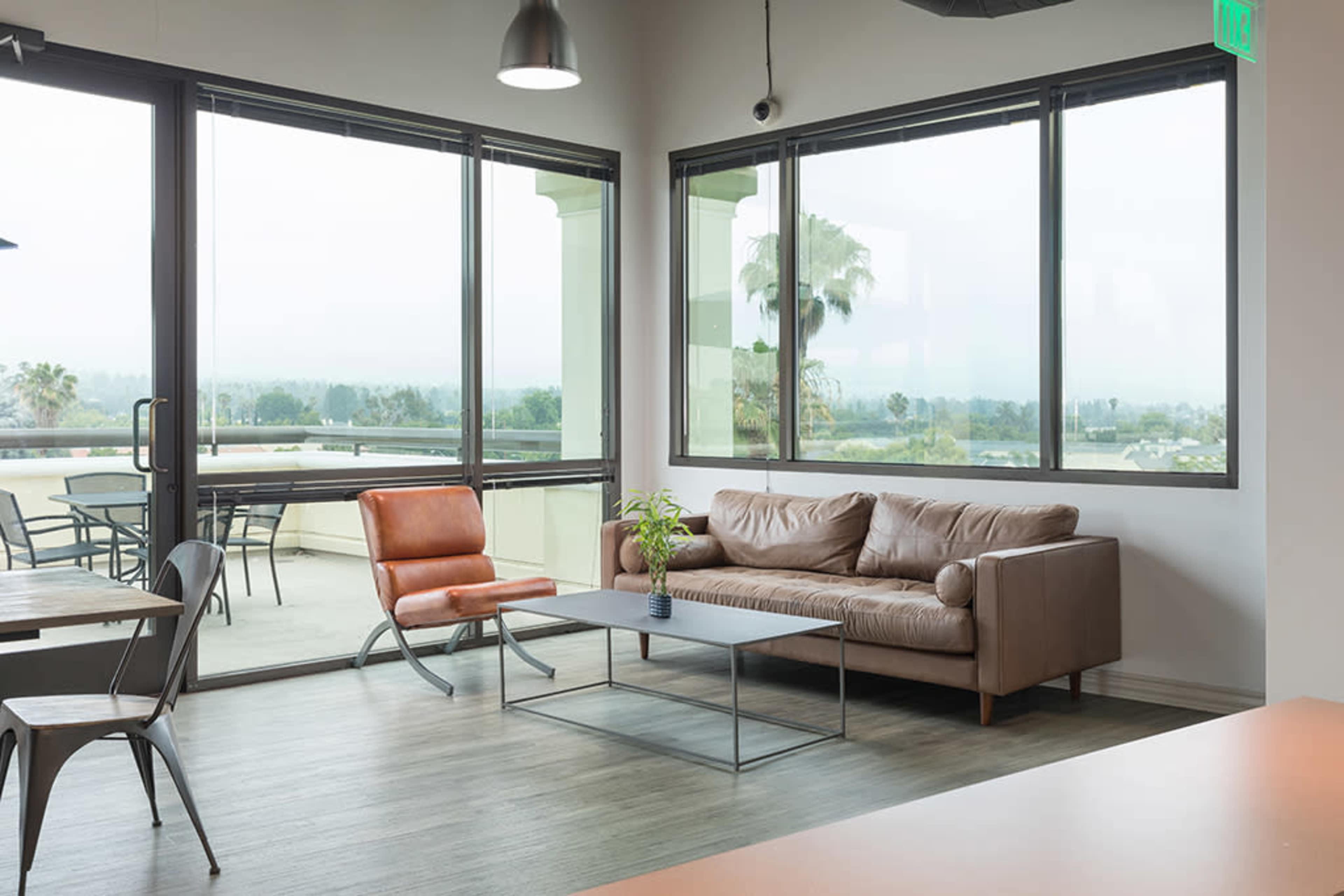 A modern indoor seating area with a brown leather sofa, a metal coffee table, and large windows providing a view of the outside.
