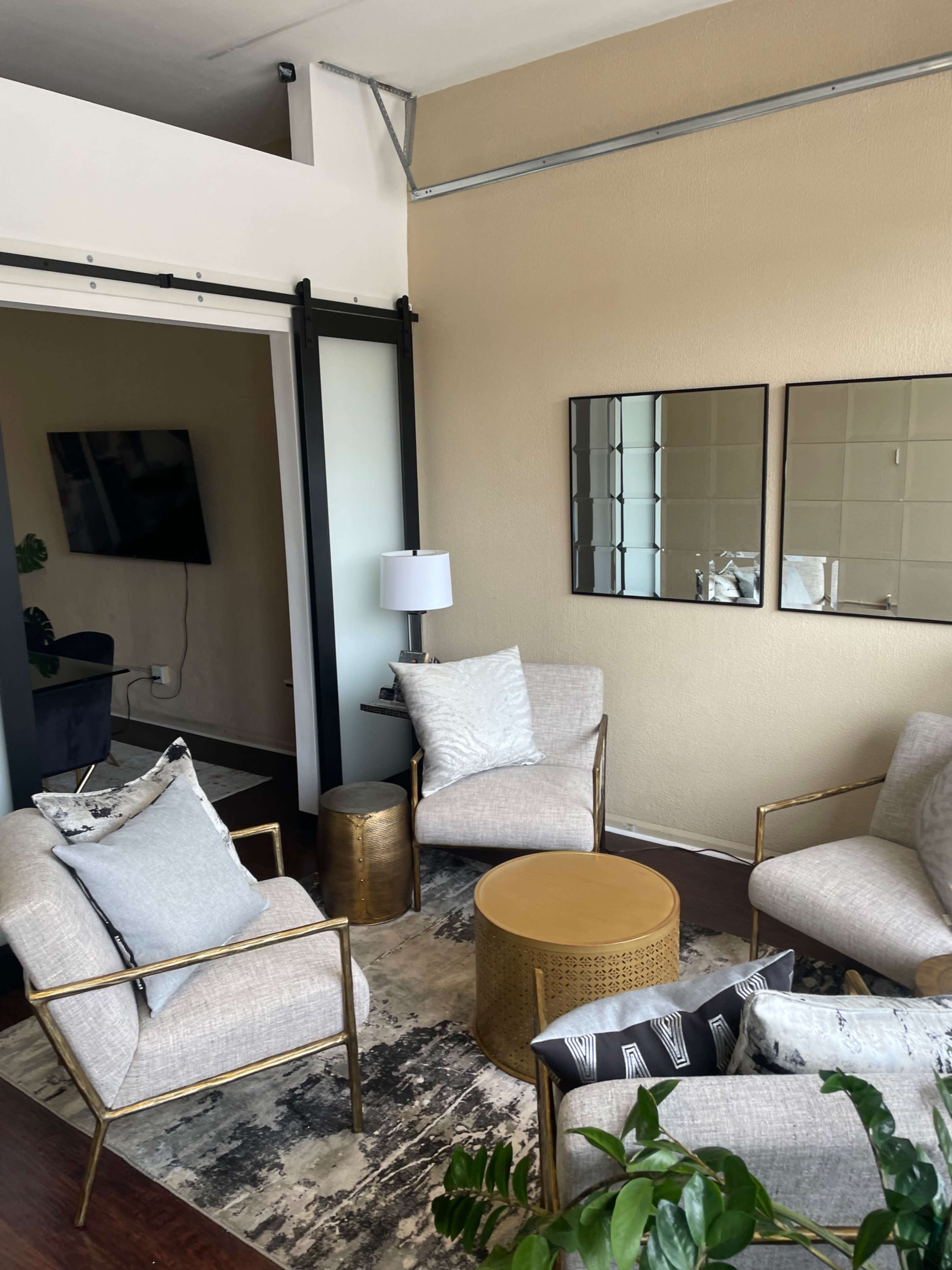 A modern living room features four chairs arranged around a round coffee table, with a lamp and mirrors on the wall.