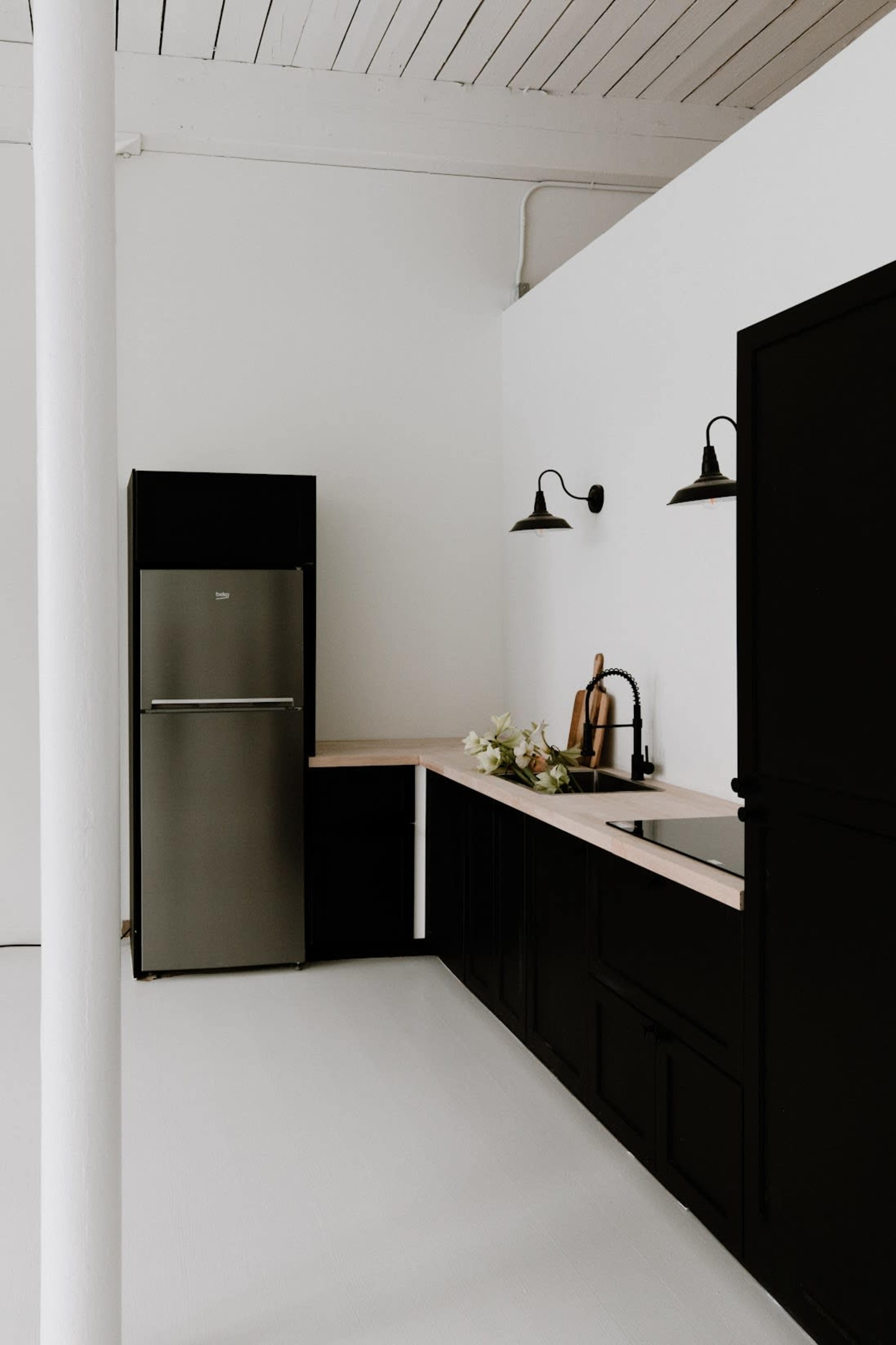A modern kitchen features a stainless steel refrigerator, black cabinetry, and a wooden countertop with a sink and wall-mounted lights.