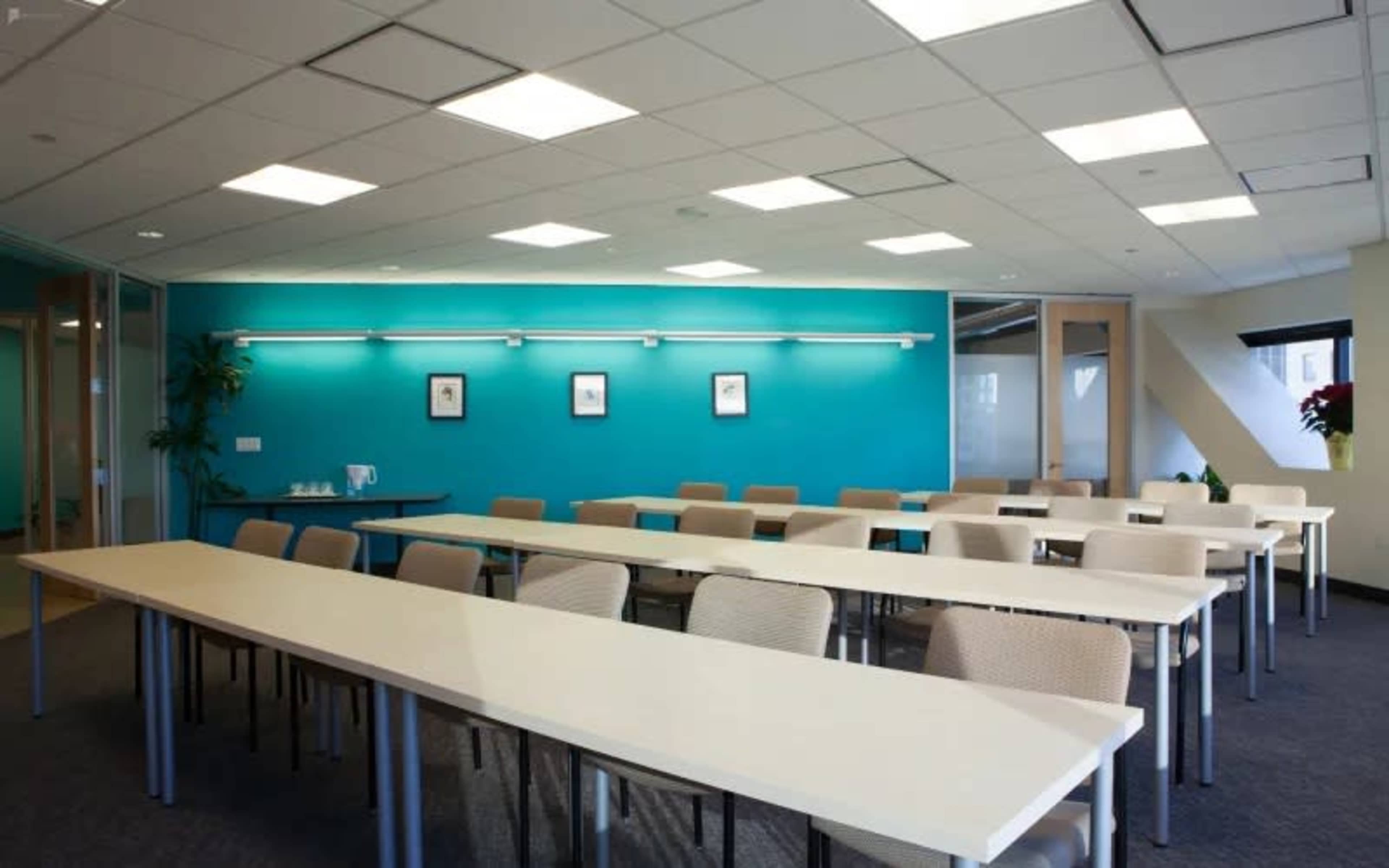 A modern conference room features long tables arranged in a U-shape, with beige chairs and a vibrant blue accent wall.