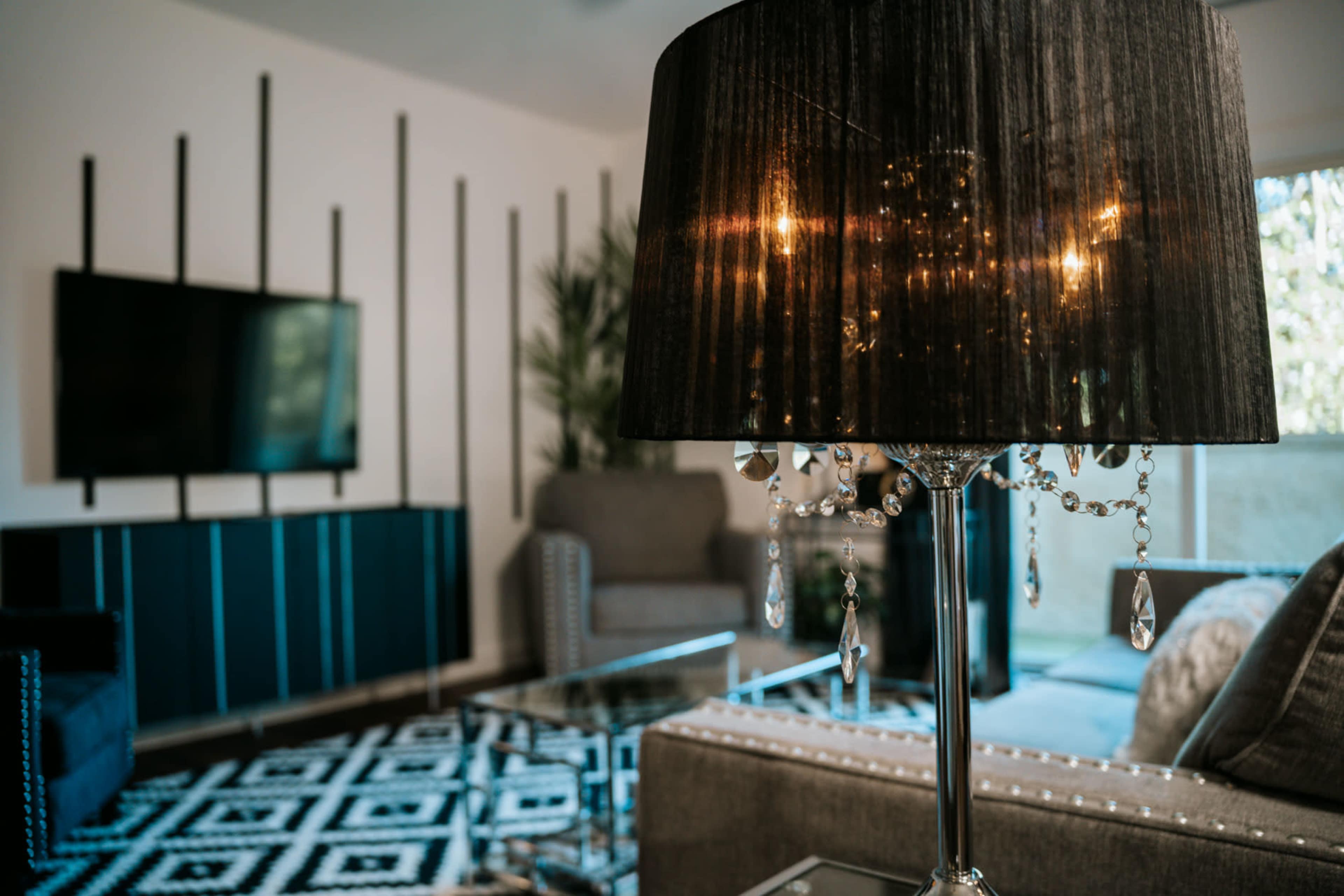 A stylish living room features a lamp with a black shade and crystal accents, surrounded by modern furniture and a geometric patterned rug.
