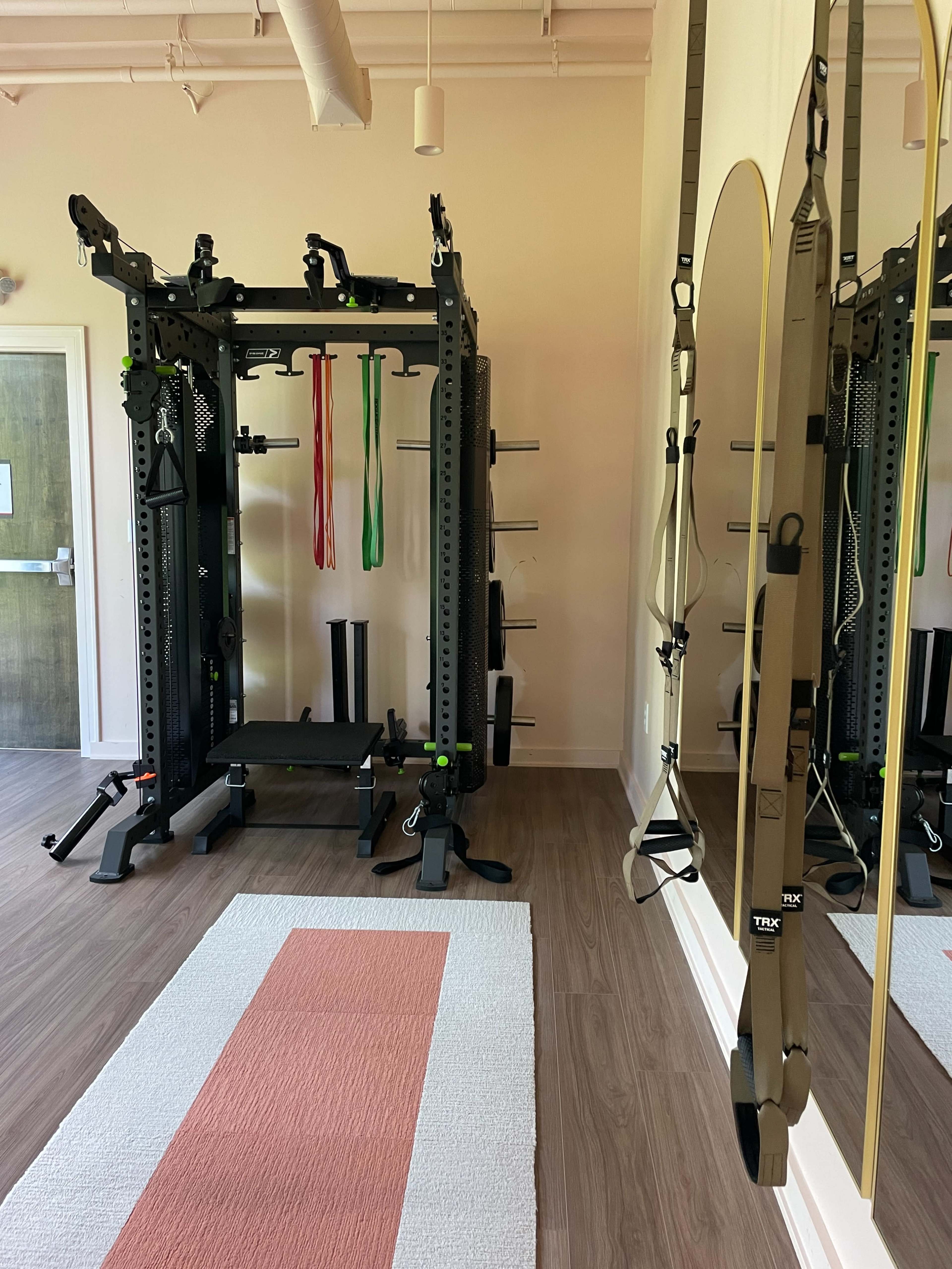 The image shows a well-equipped home gym featuring a power rack with resistance bands, a bench, and exercise straps mounted on the wall.