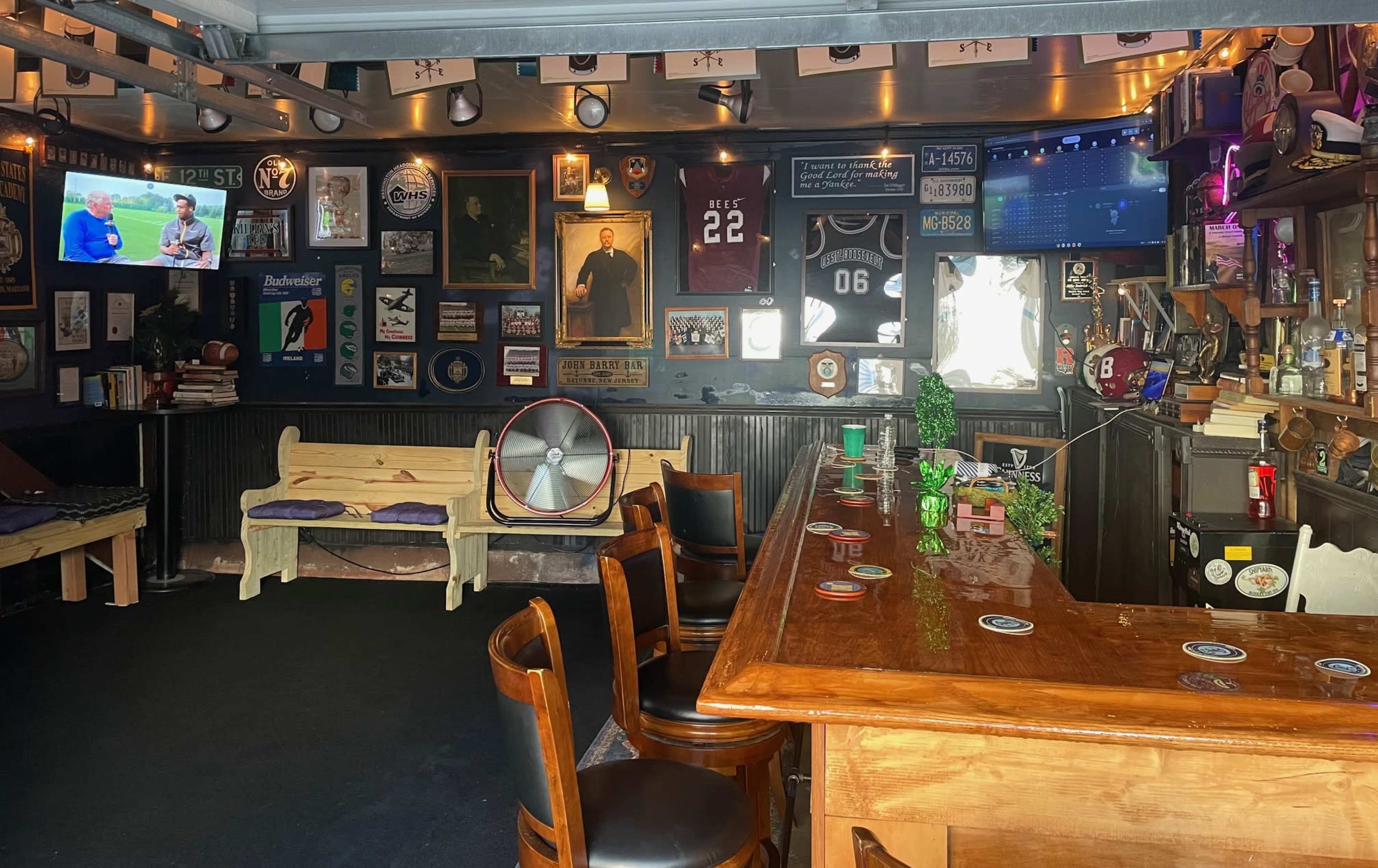The image shows a cozy bar setup with a wooden counter, several bar stools, and various framed memorabilia and decorations on the walls.