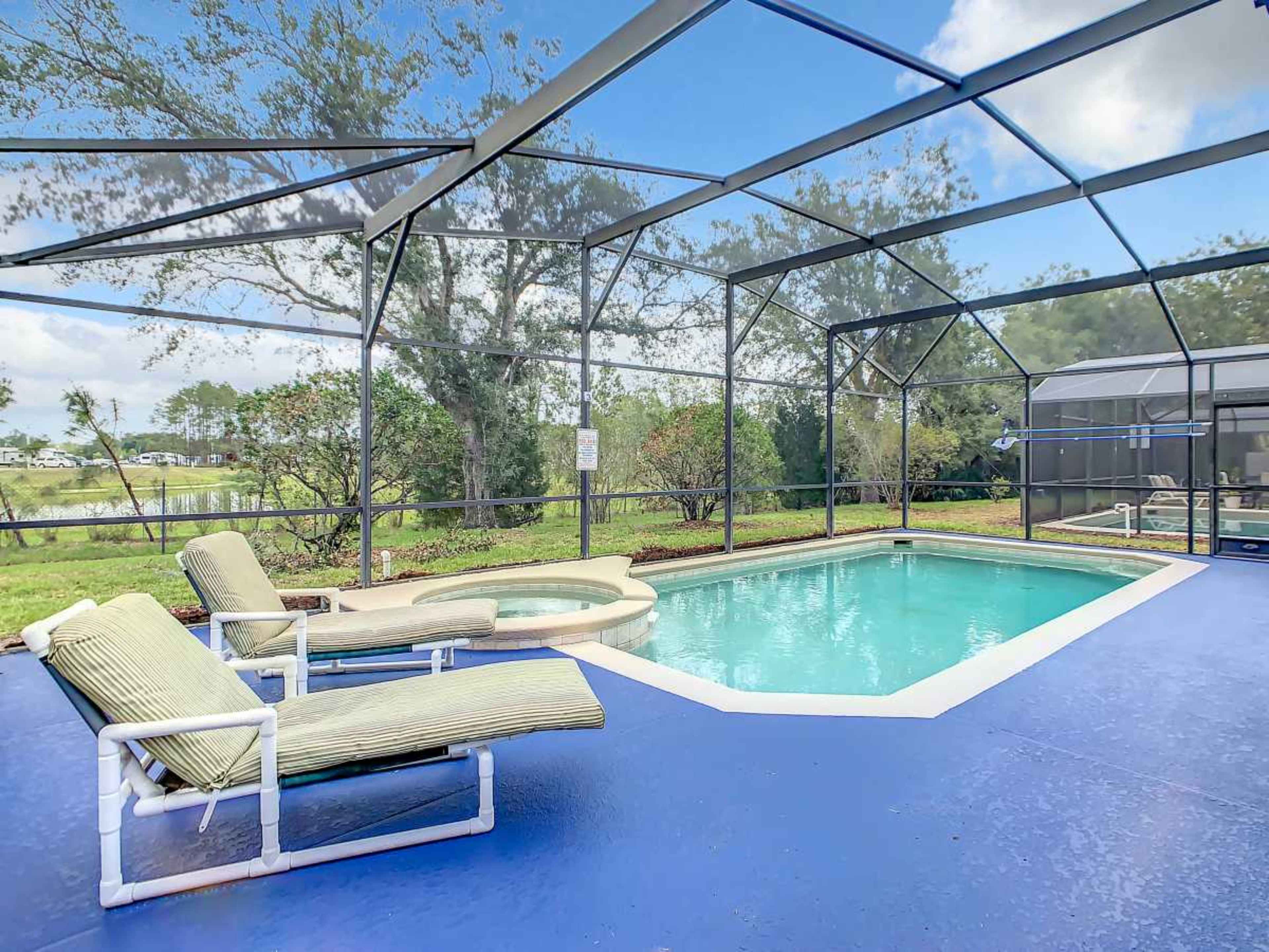The image shows a screened-in pool area with two lounge chairs next to a swimming pool, surrounded by greenery and blue skies.