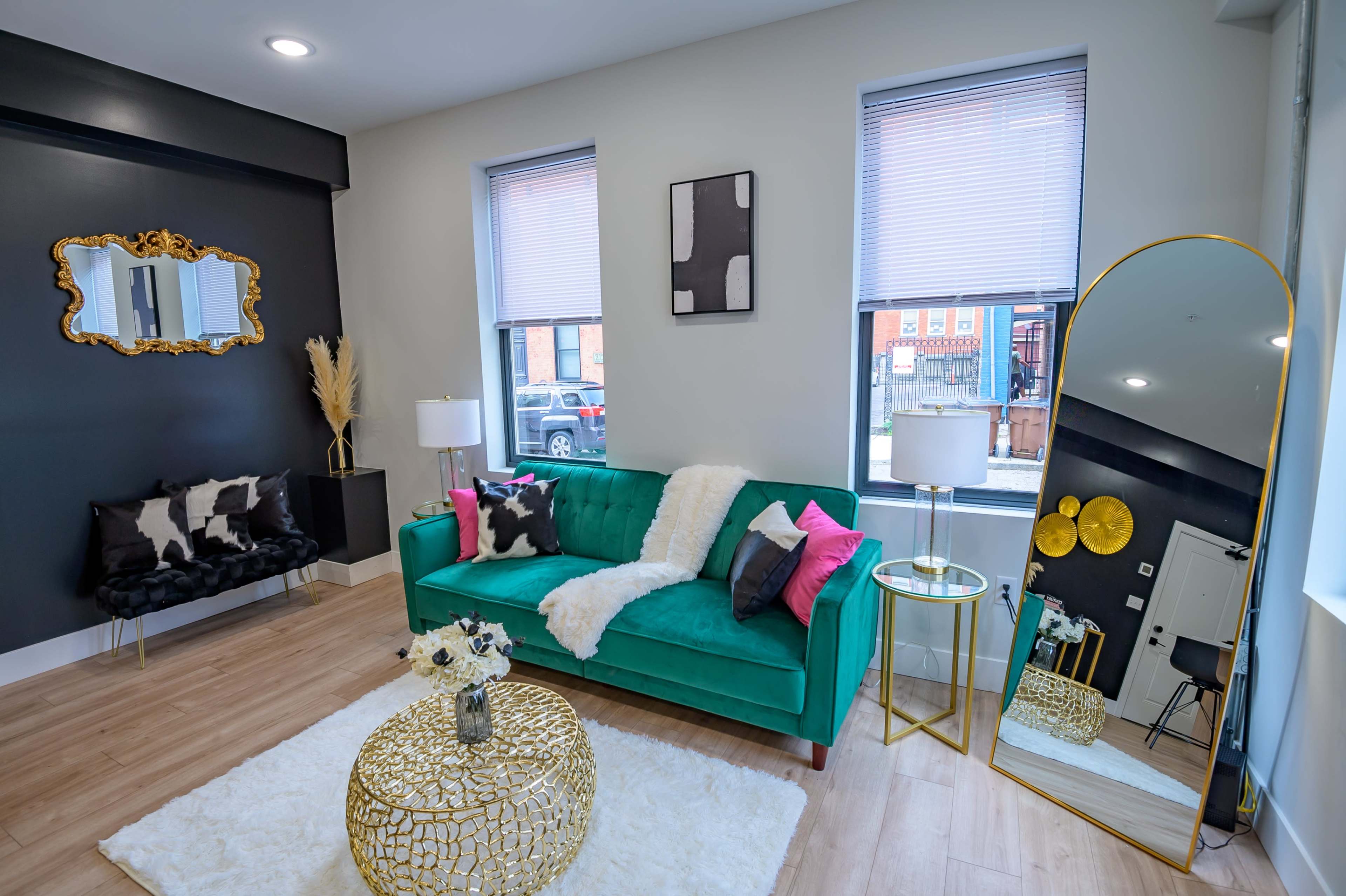 A stylish living room features a green couch, a round gold coffee table, and a large mirror against a gray wall.