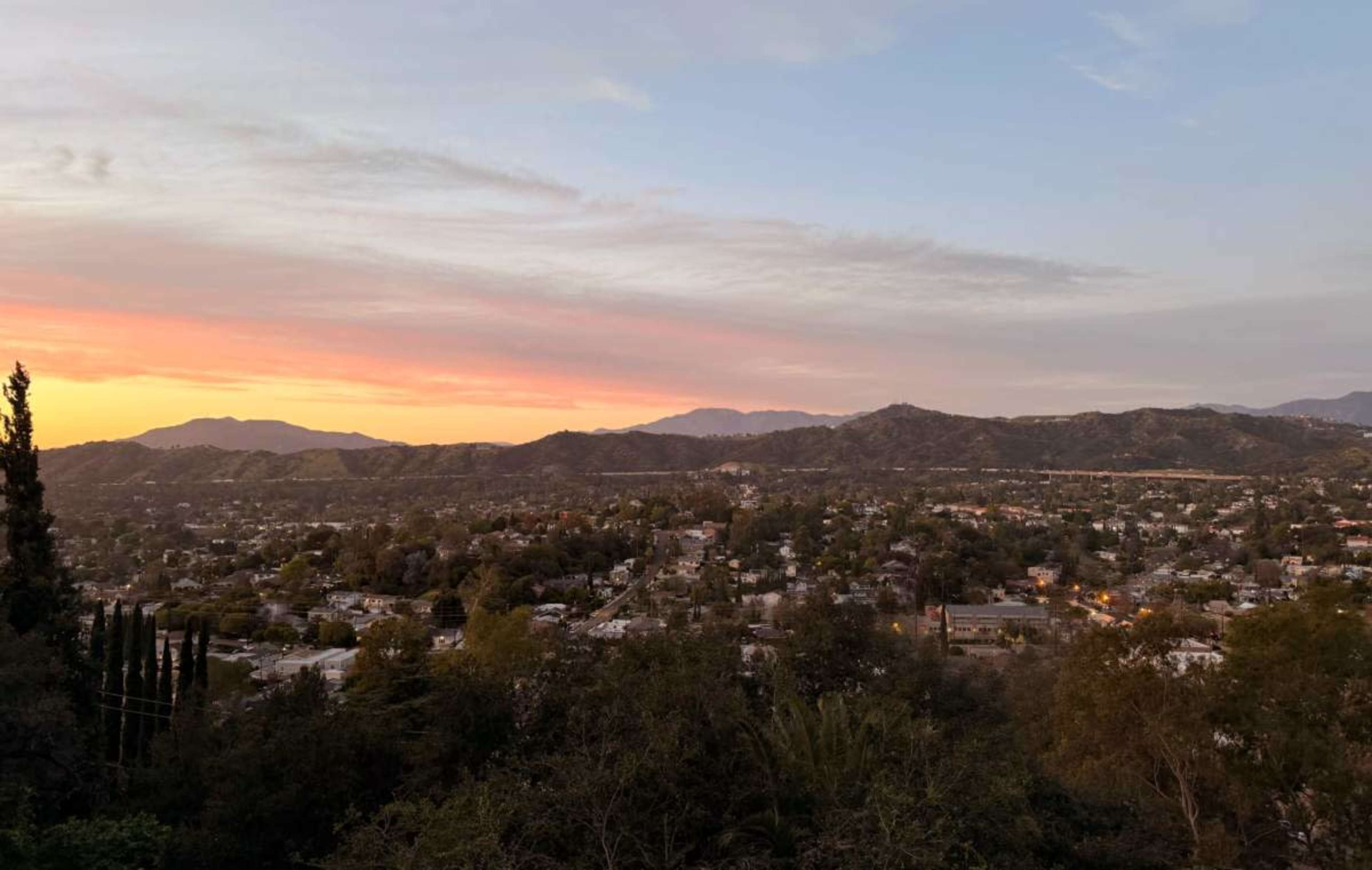 The image shows a sunset over a mountainous landscape with a sprawling town nestled in the valley.