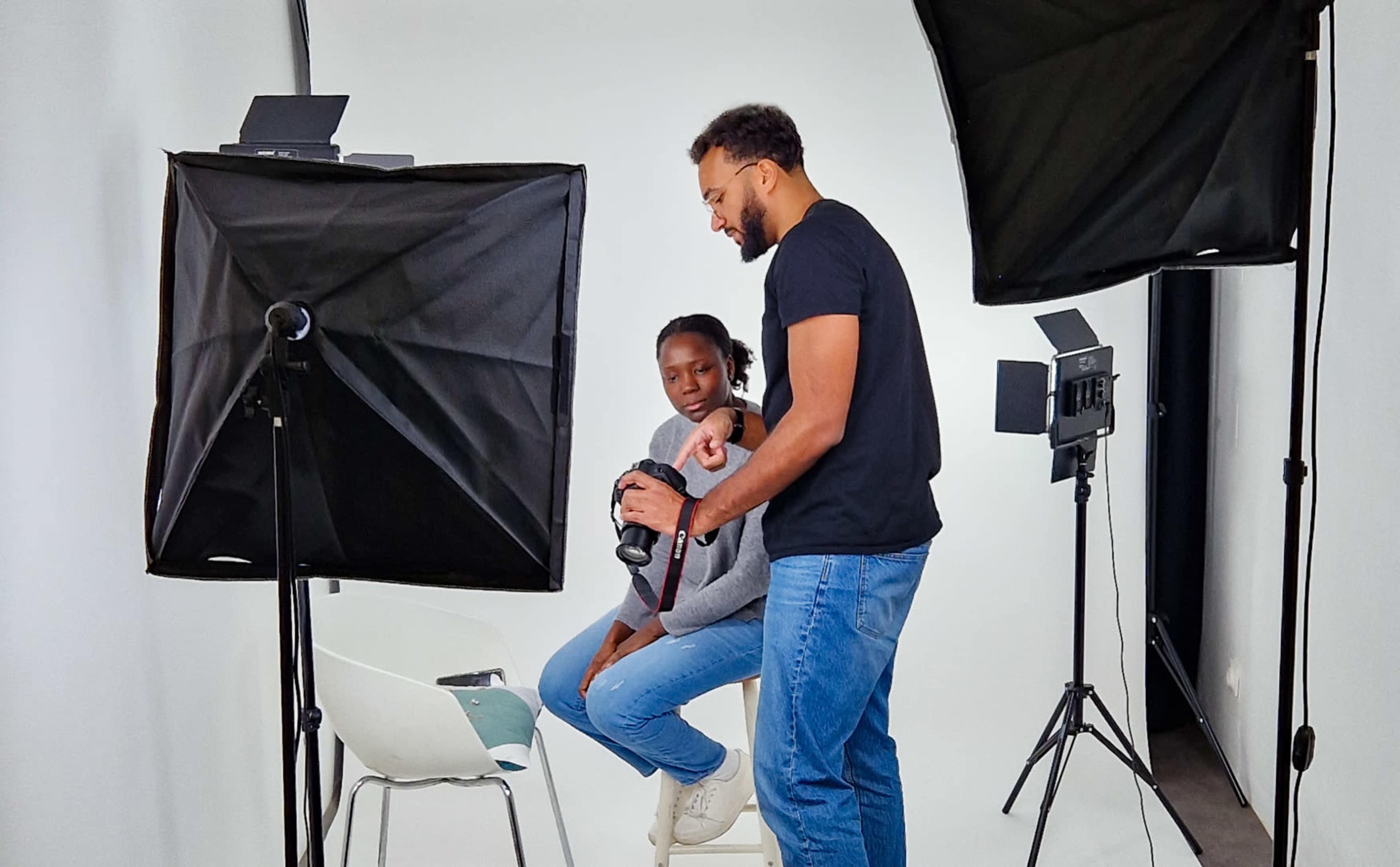 A photographer adjusts the settings on a camera while a young girl sits on a stool in a well-lit studio.