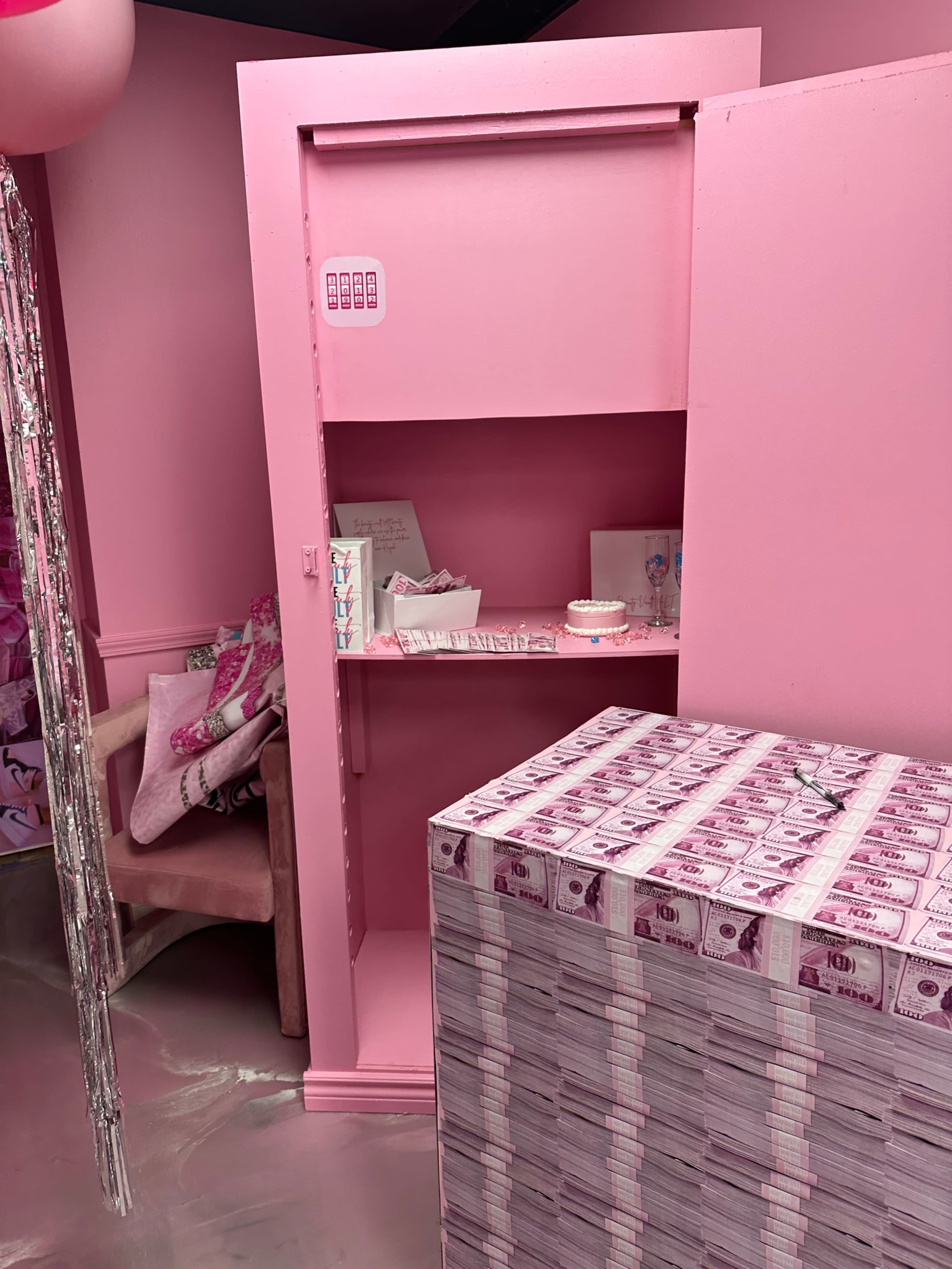 A pink room featuring a large stack of faux money and an open pink cabinet with a few items displayed inside.