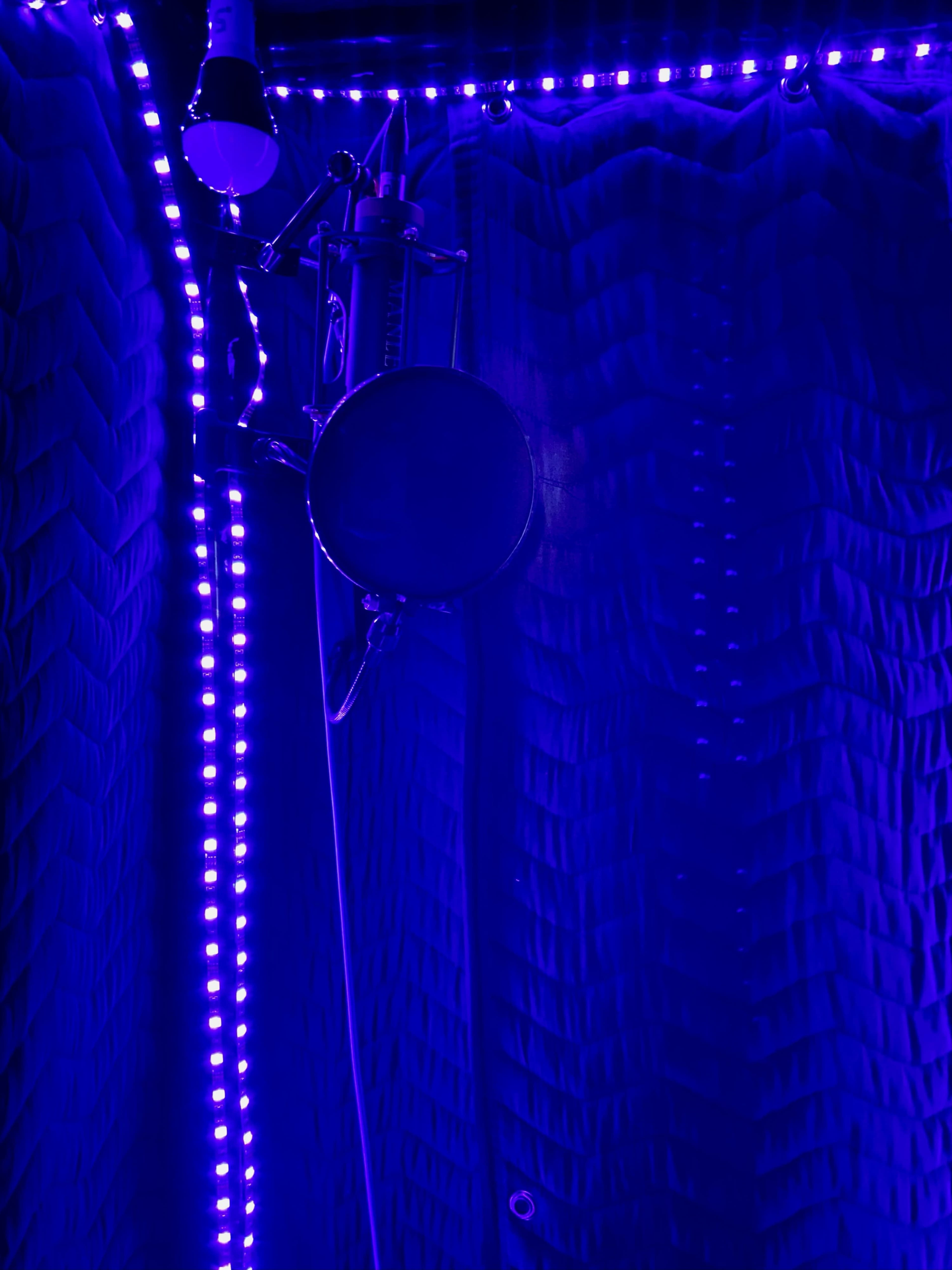 The image shows a microphone set up in a soundproof booth illuminated by purple LED lights.