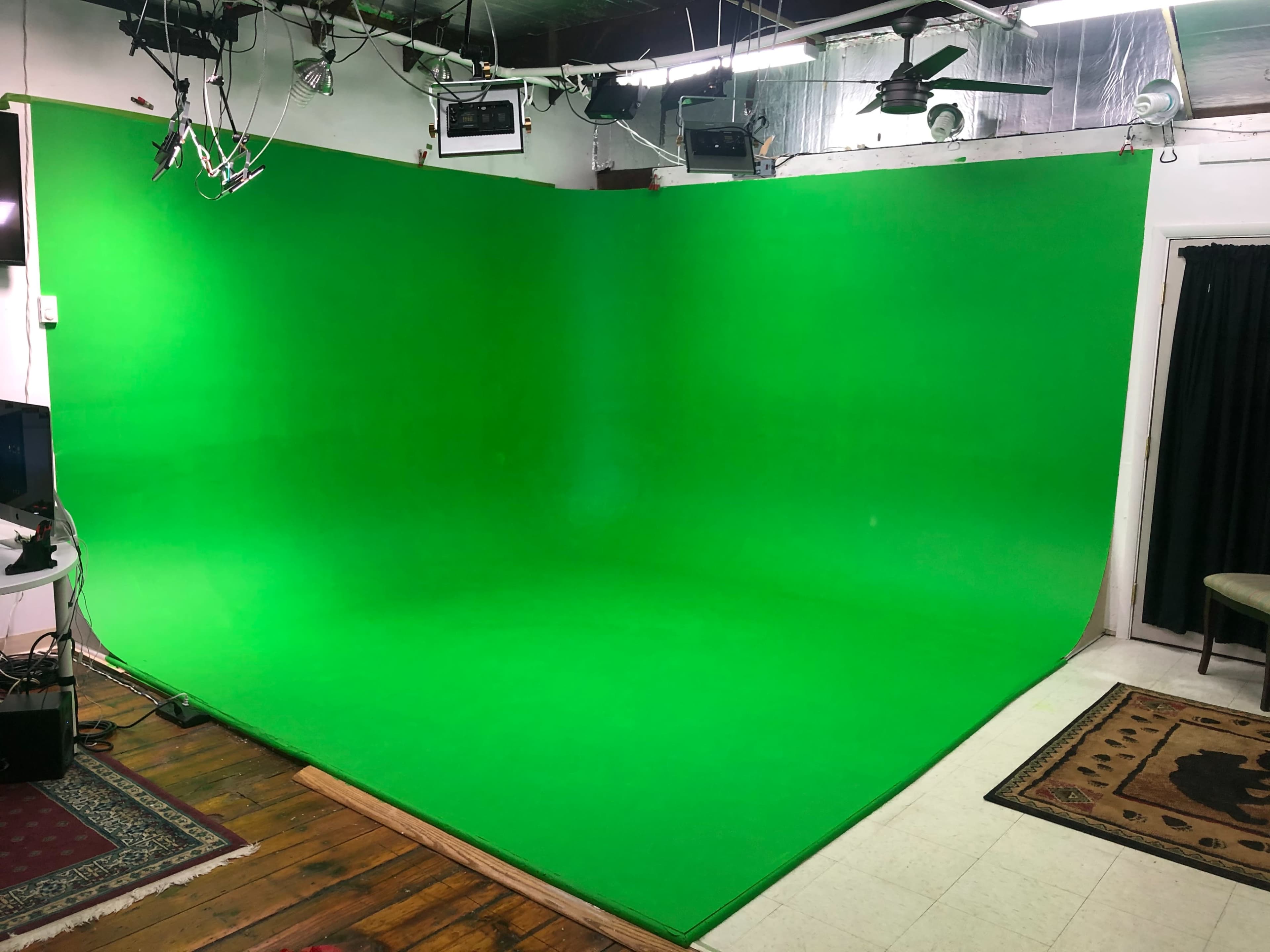 A green screen studio with a curved green backdrop and various lighting and equipment set up around it.