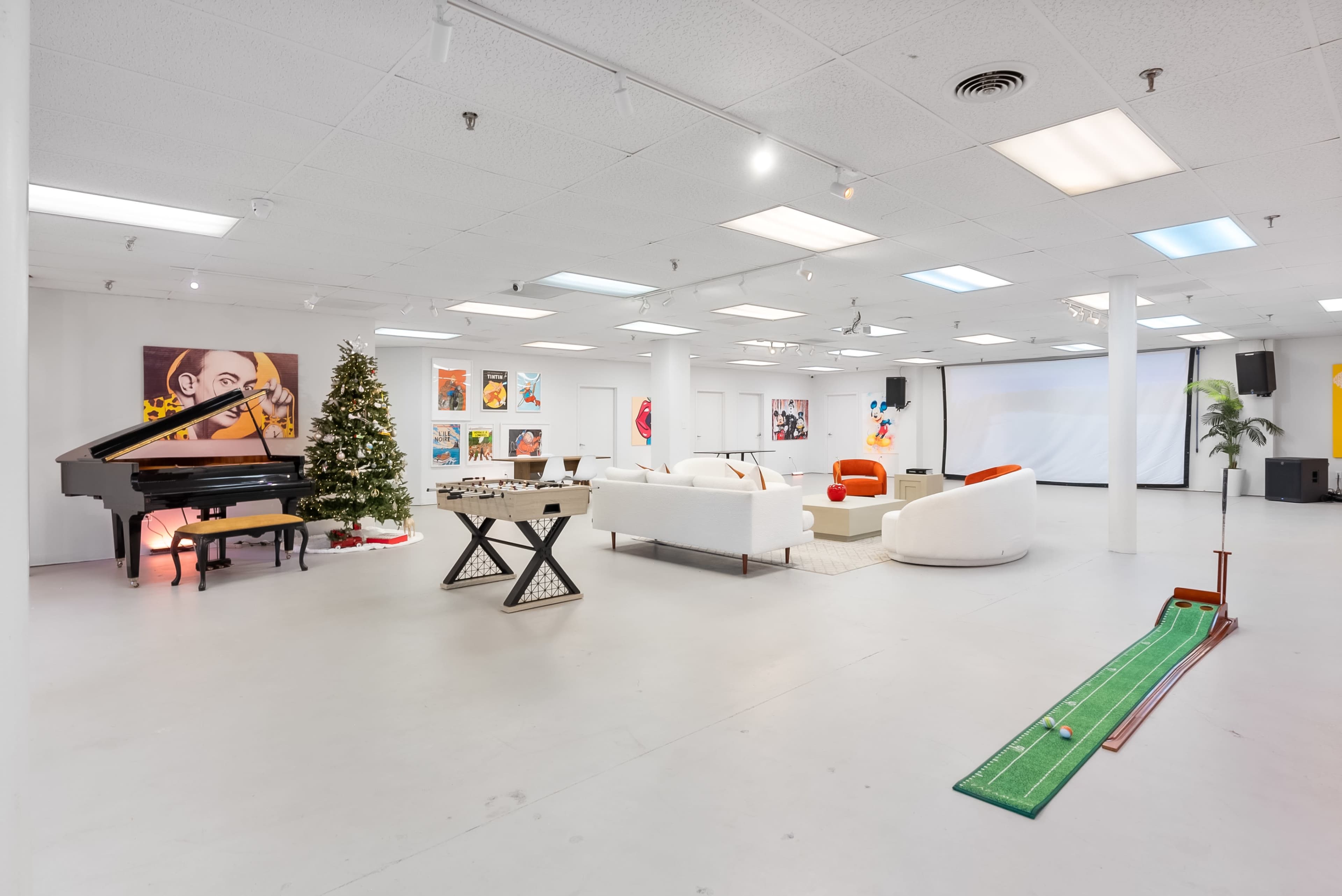 The image shows a spacious indoor area featuring a grand piano, a Christmas tree, a white sectional sofa, colorful artwork on the walls, and a putting green on the floor.