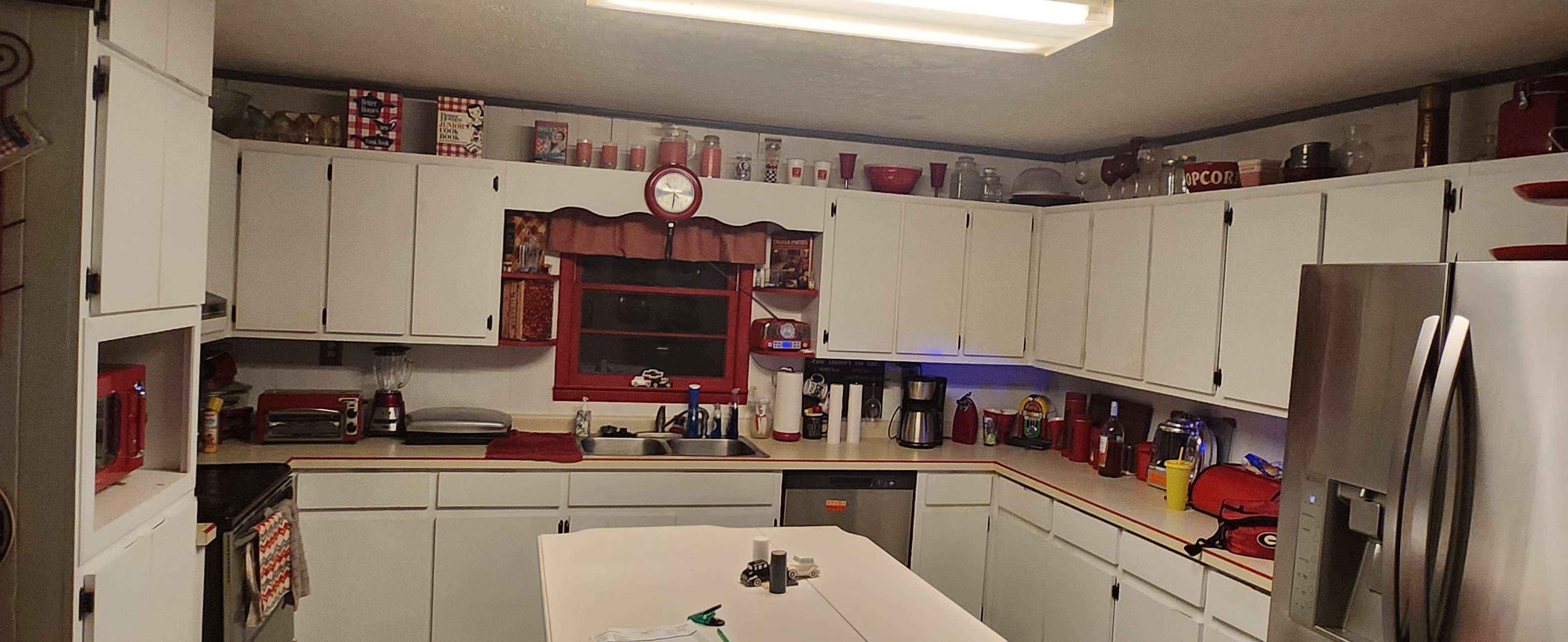 A kitchen features white cabinetry, a central island, and various kitchen appliances with a red and silver color scheme.
