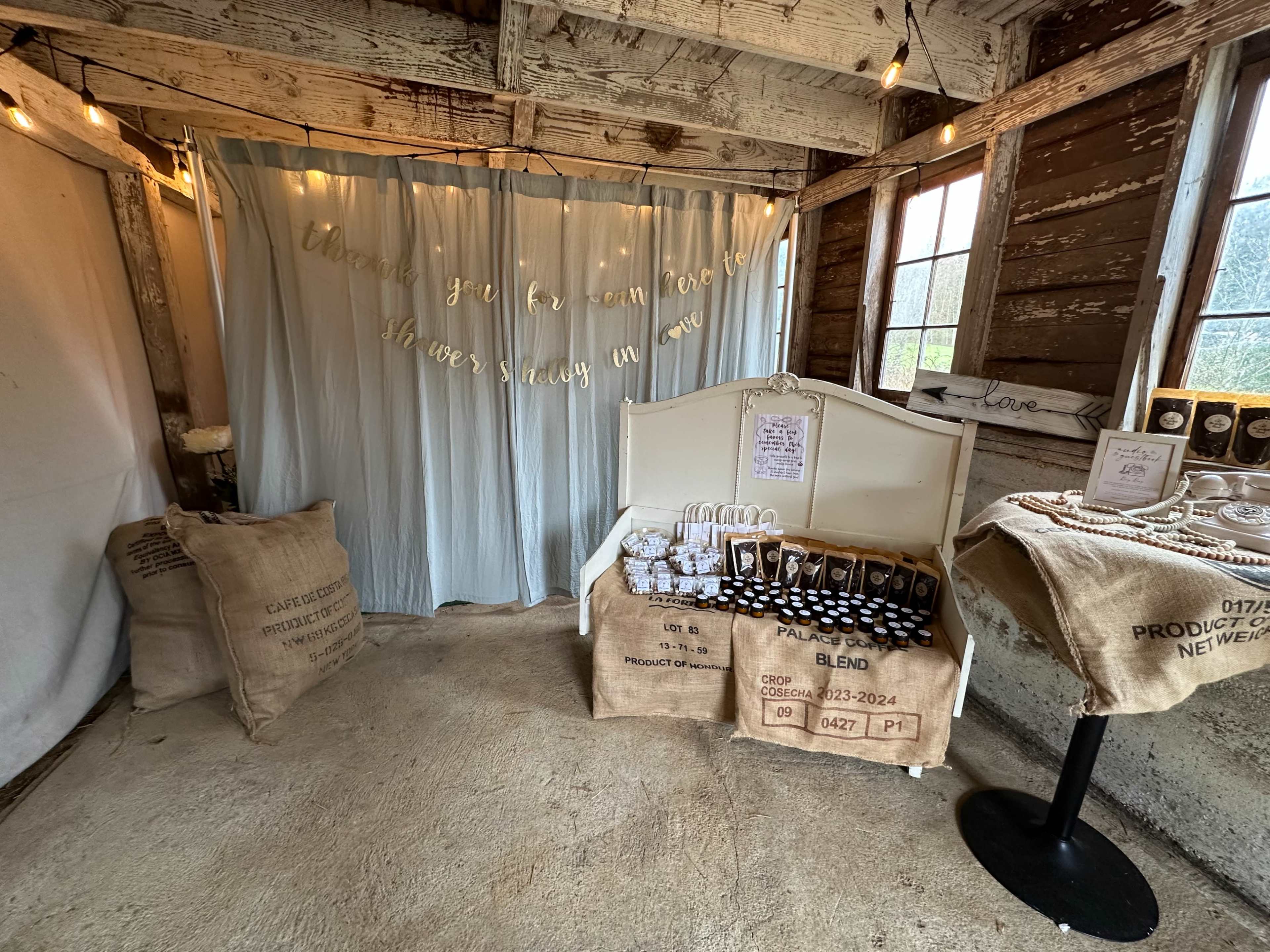 The image shows a rustic indoor space with a decorative light blue curtain and a small display of packaged items, including bags and jewelry, set against a wooden wall.