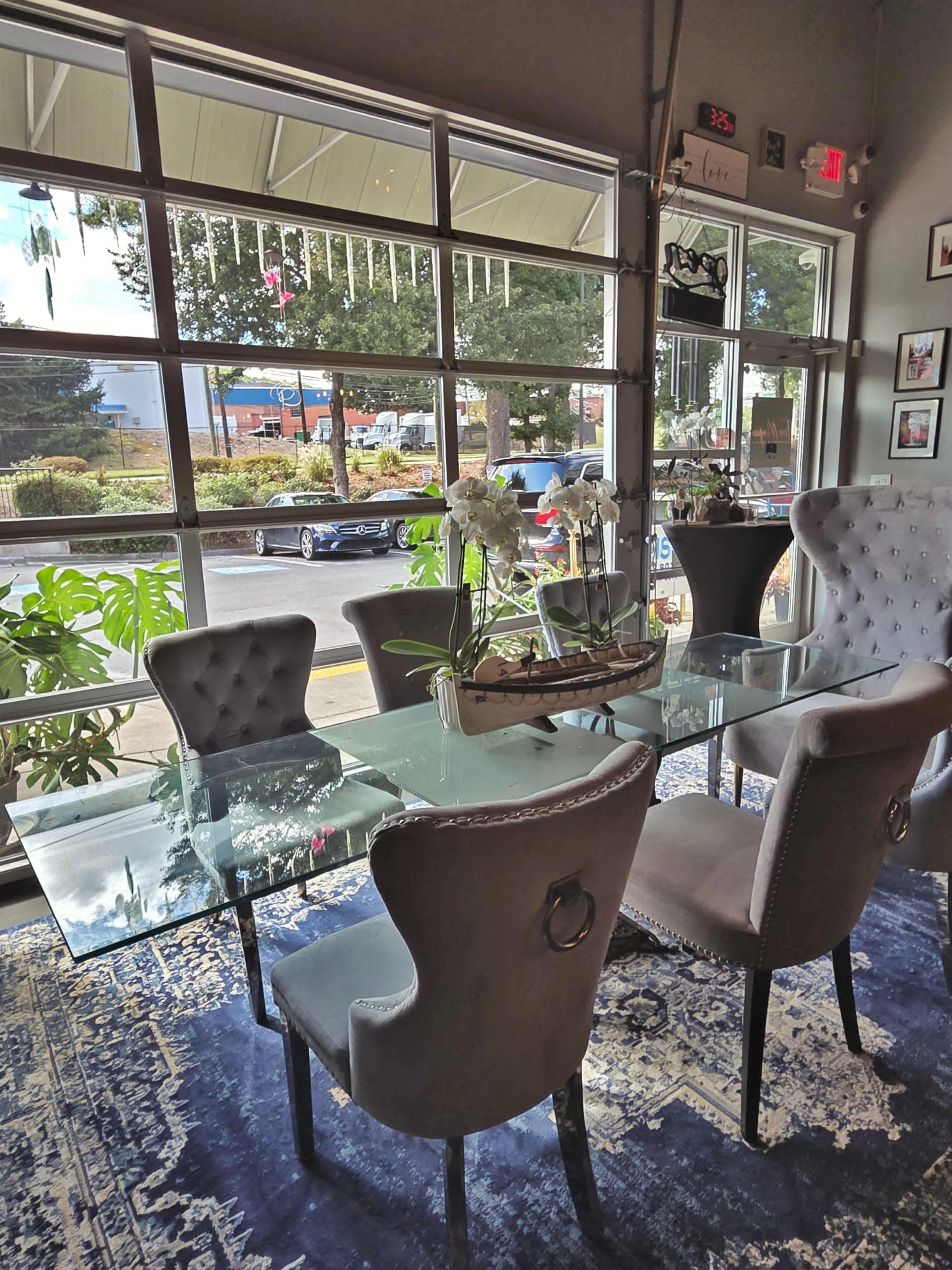 The image shows a well-lit dining area with glass-top tables and grey upholstered chairs, overlooking a view of a street through large windows.