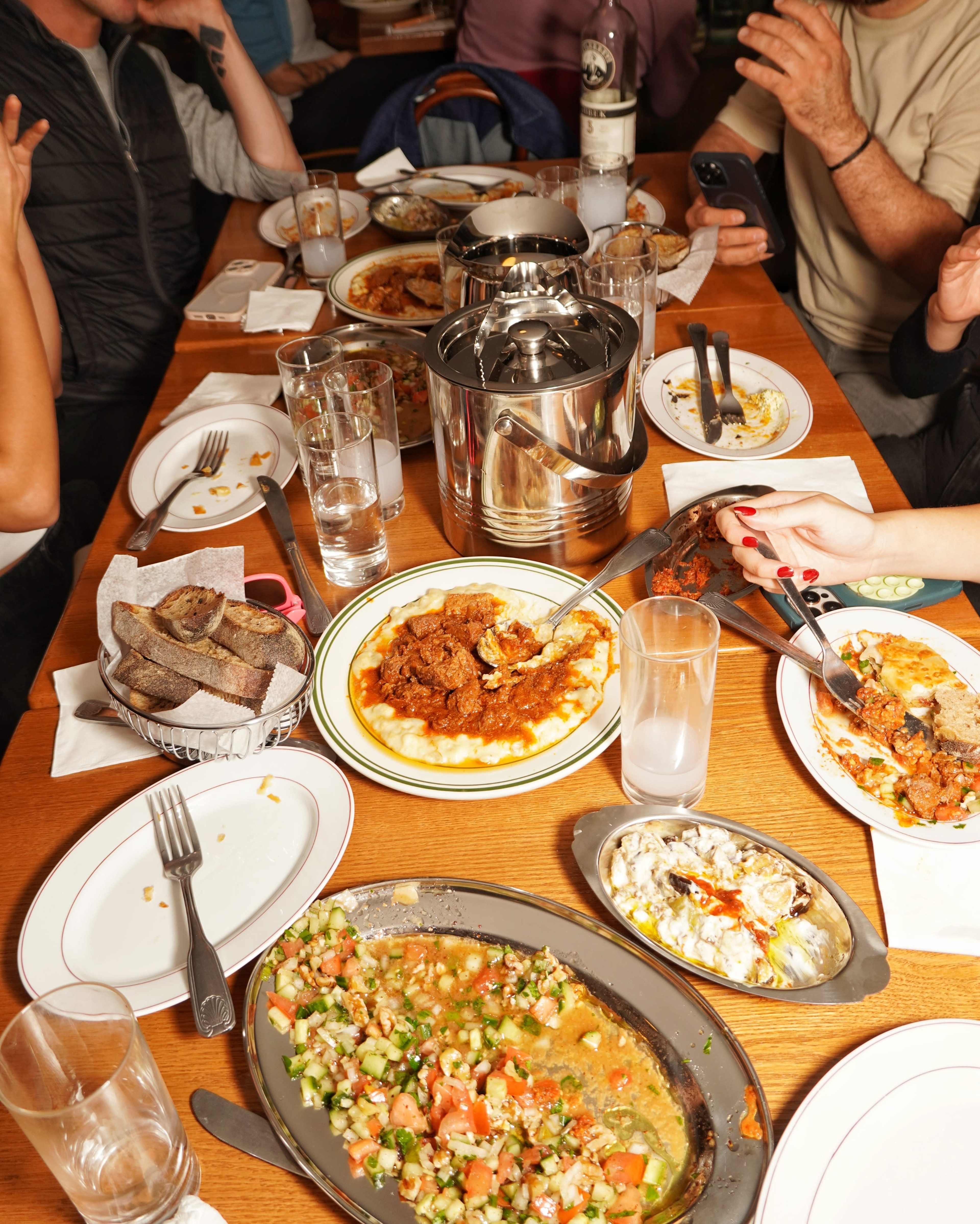 The table is cluttered with various dishes, drinks, and utensils after a meal, showcasing half-eaten plates and empty glasses.