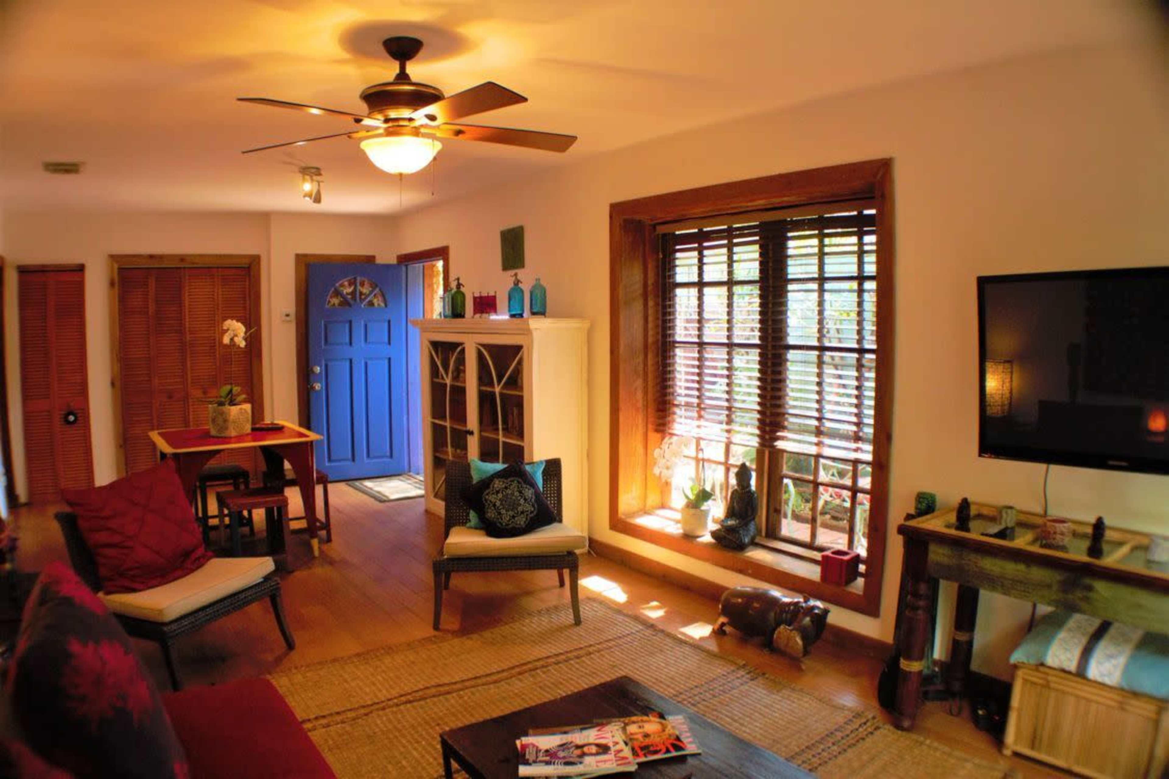 A living room with a blue front door, a wooden table, a seating area, and a window featuring wooden blinds and decorative items.