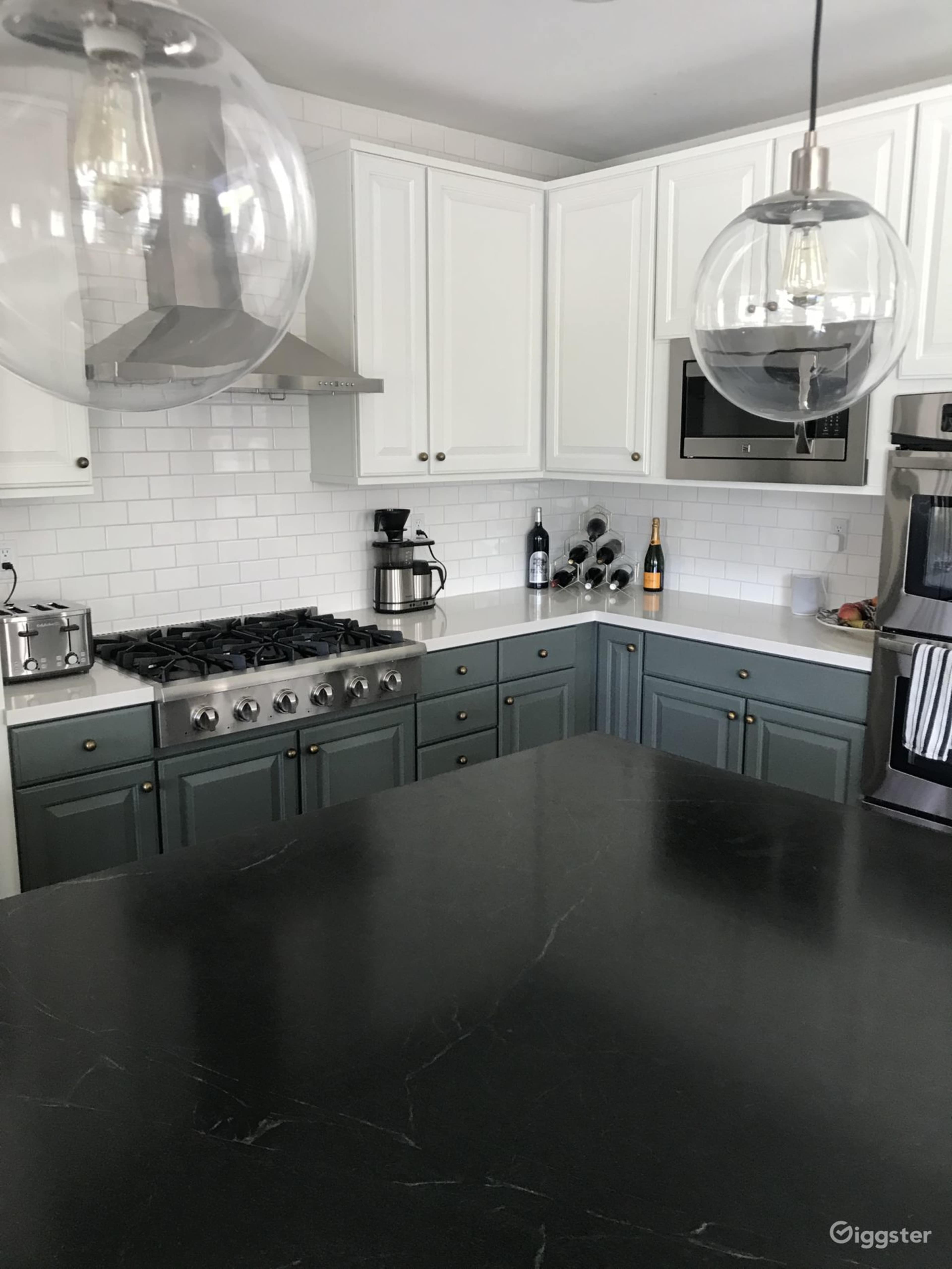 The kitchen features white cabinetry, a dark countertop, and stainless steel appliances, with two pendant lights hanging above the island.