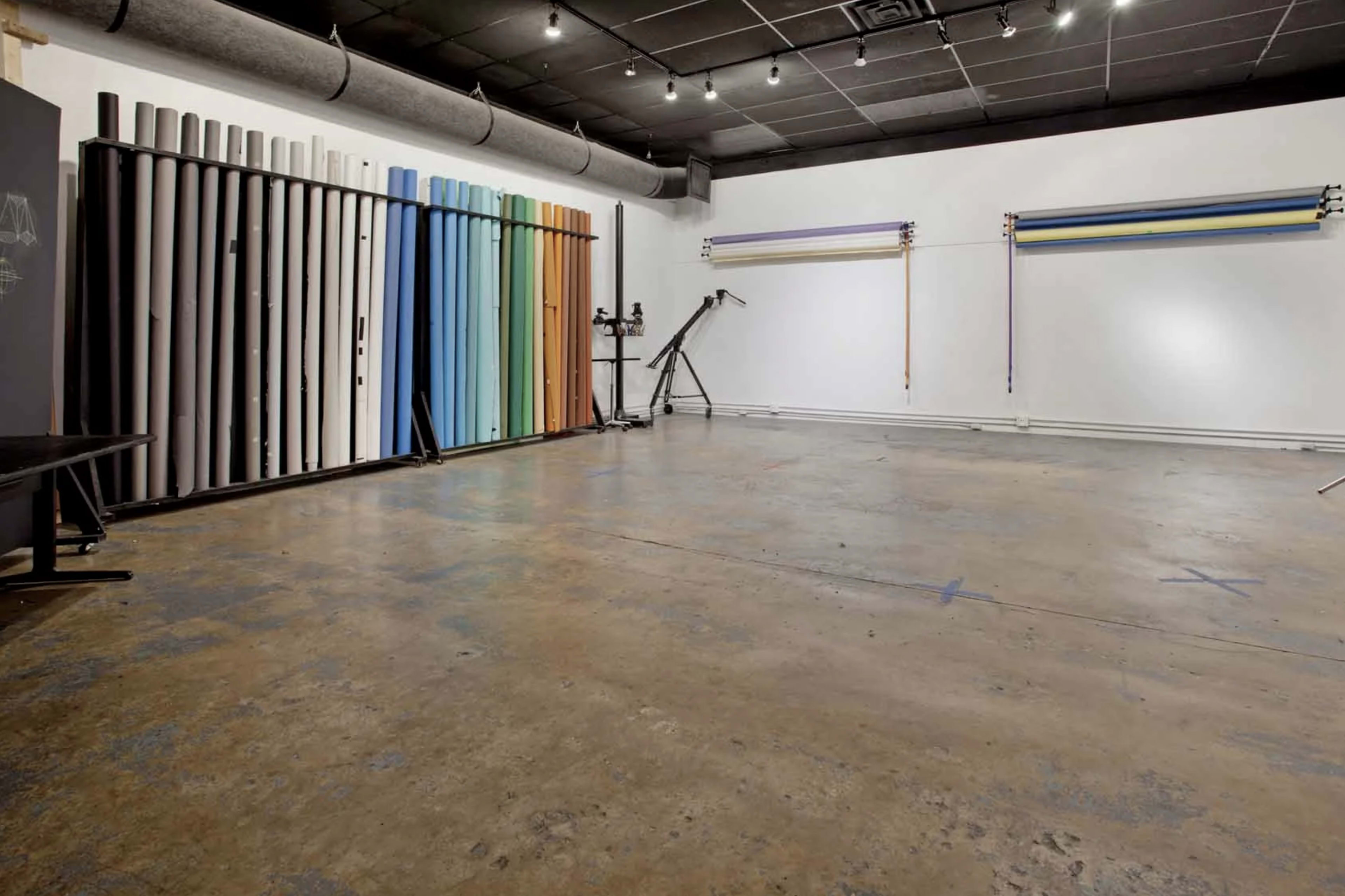 A spacious studio with a concrete floor and various colored backdrops arranged against the wall.