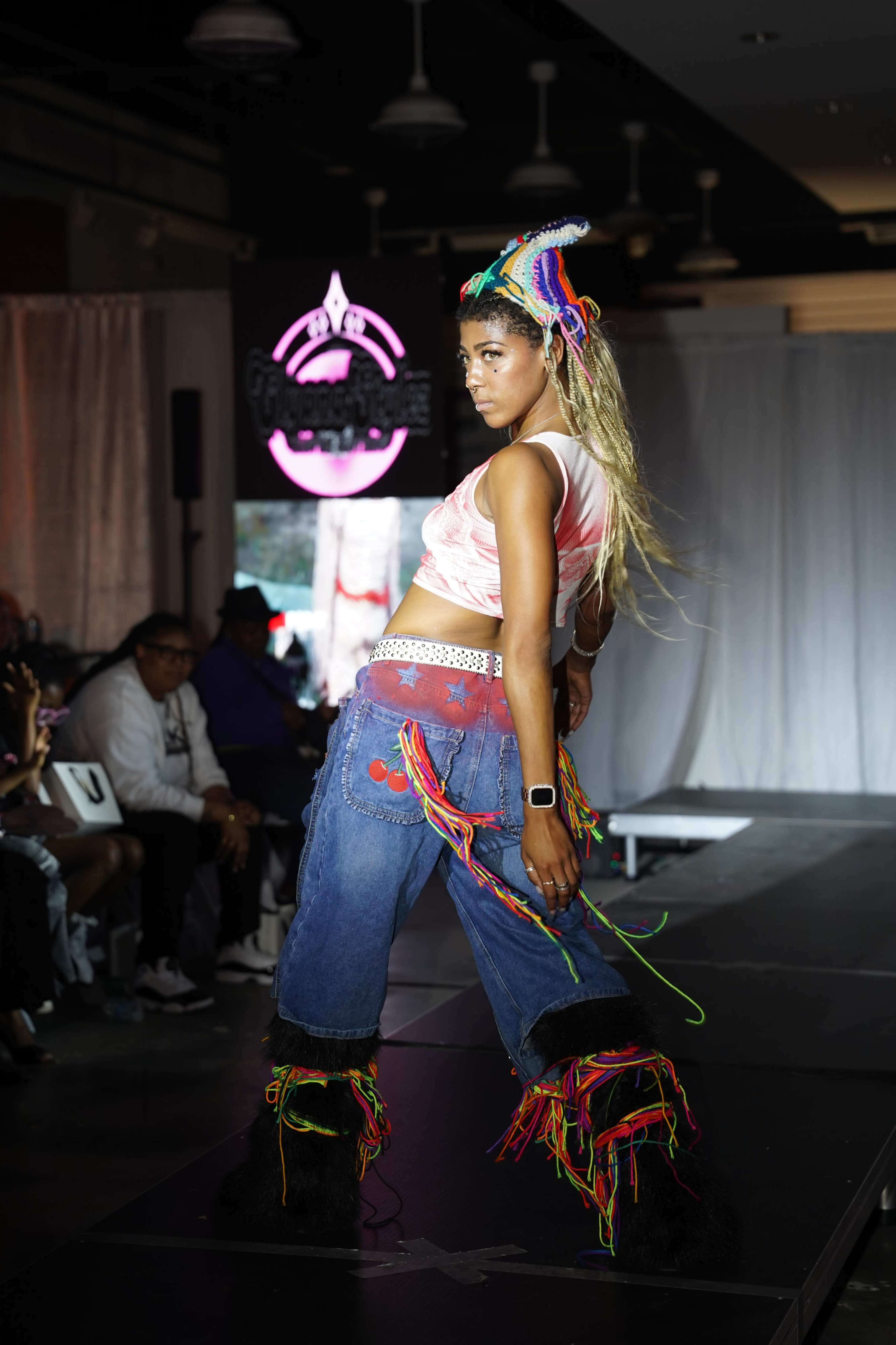 A model walks down the runway wearing colorful attire that features fringe and vibrant accessories.