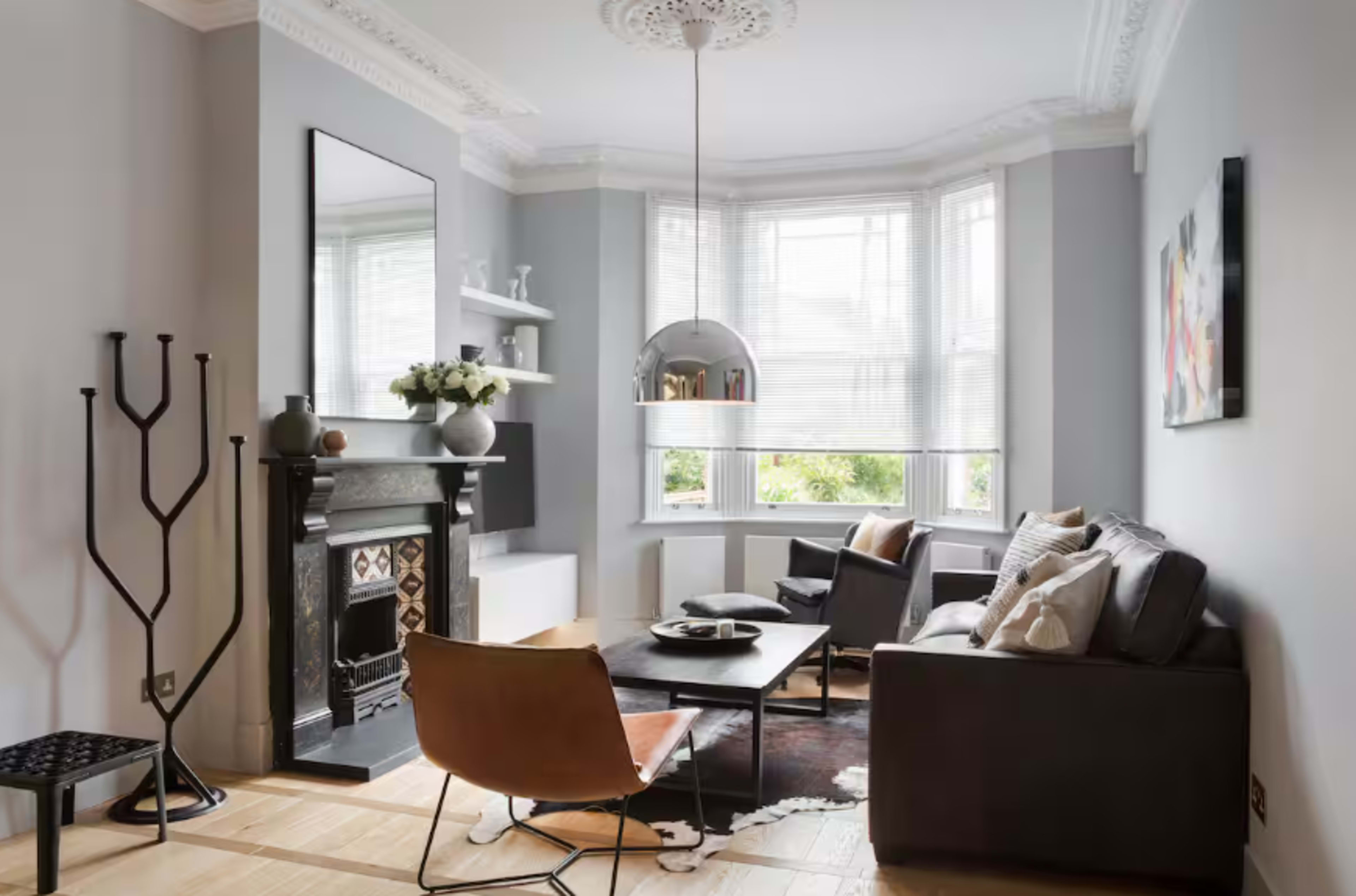 The image shows a modern living room with a bay window, a fireplace, and minimalist furniture arranged for comfort and style.