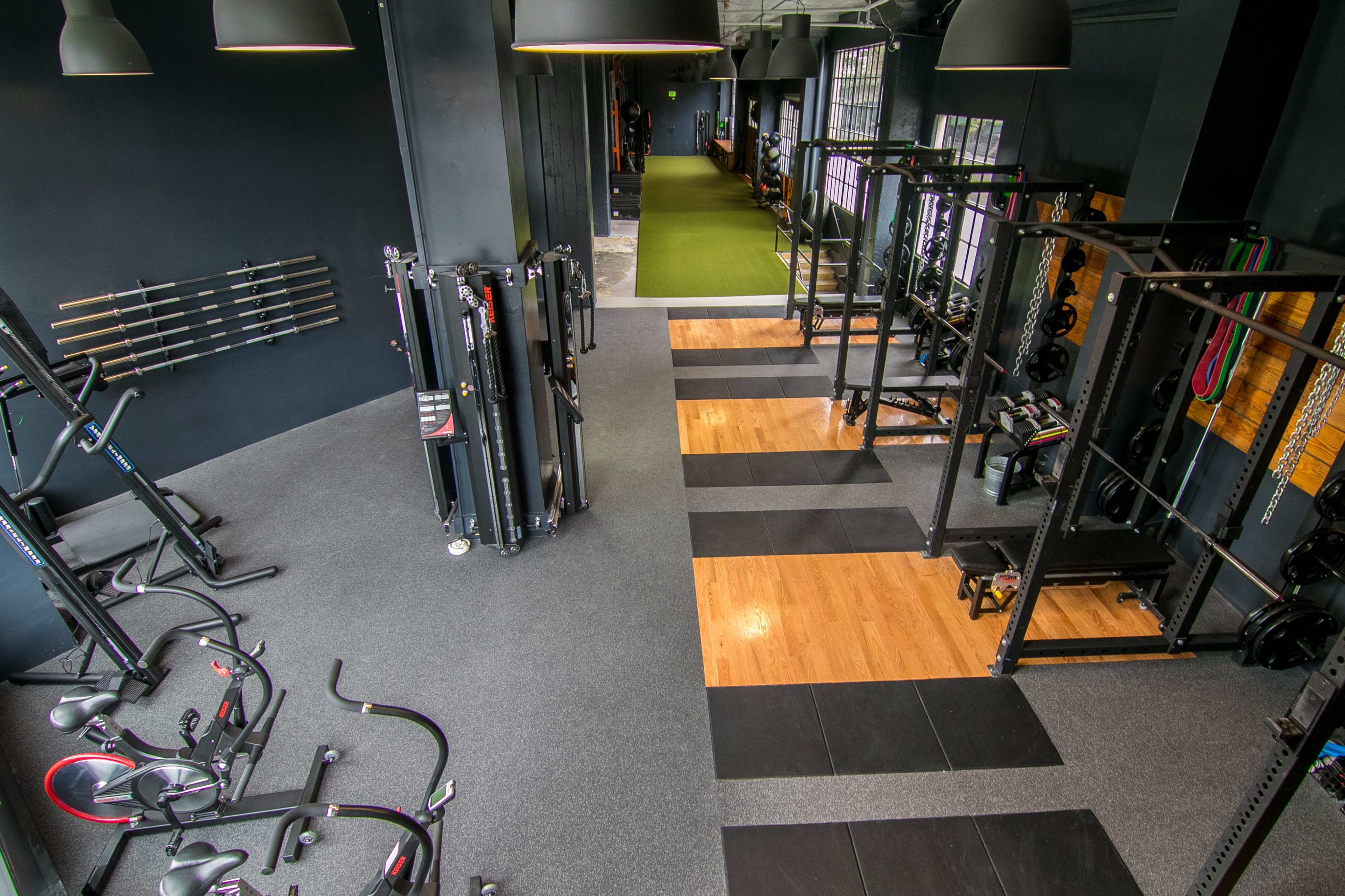 A well-organized gym layout featuring various fitness equipment and open workout spaces with a combination of rubber and wooden flooring.