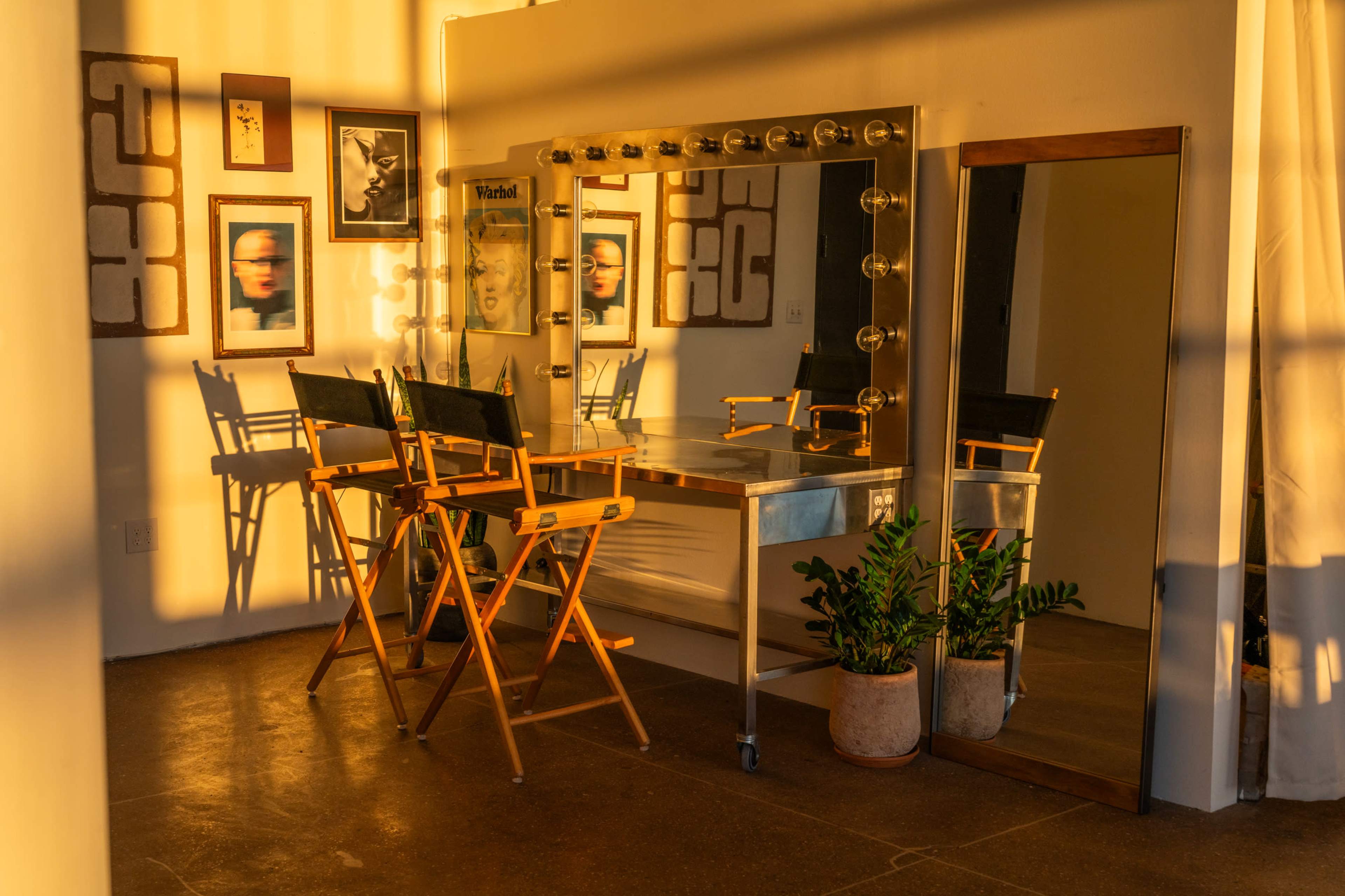 The image shows a brightly lit room with a large mirror, two director's chairs, and framed artwork on the walls.