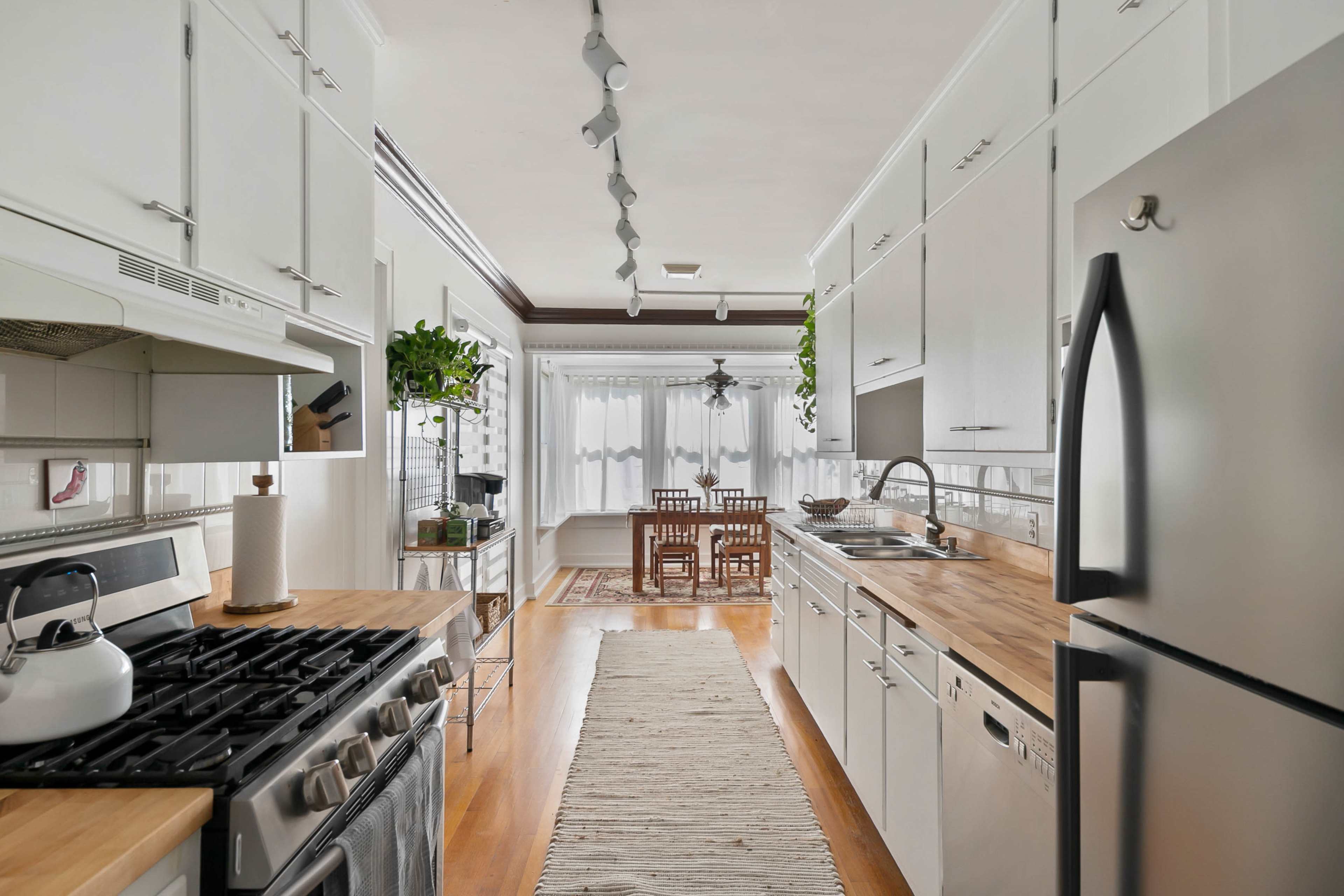 A modern kitchen features stainless steel appliances, wooden countertops, and a dining area with a wooden table and chairs bathed in natural light.