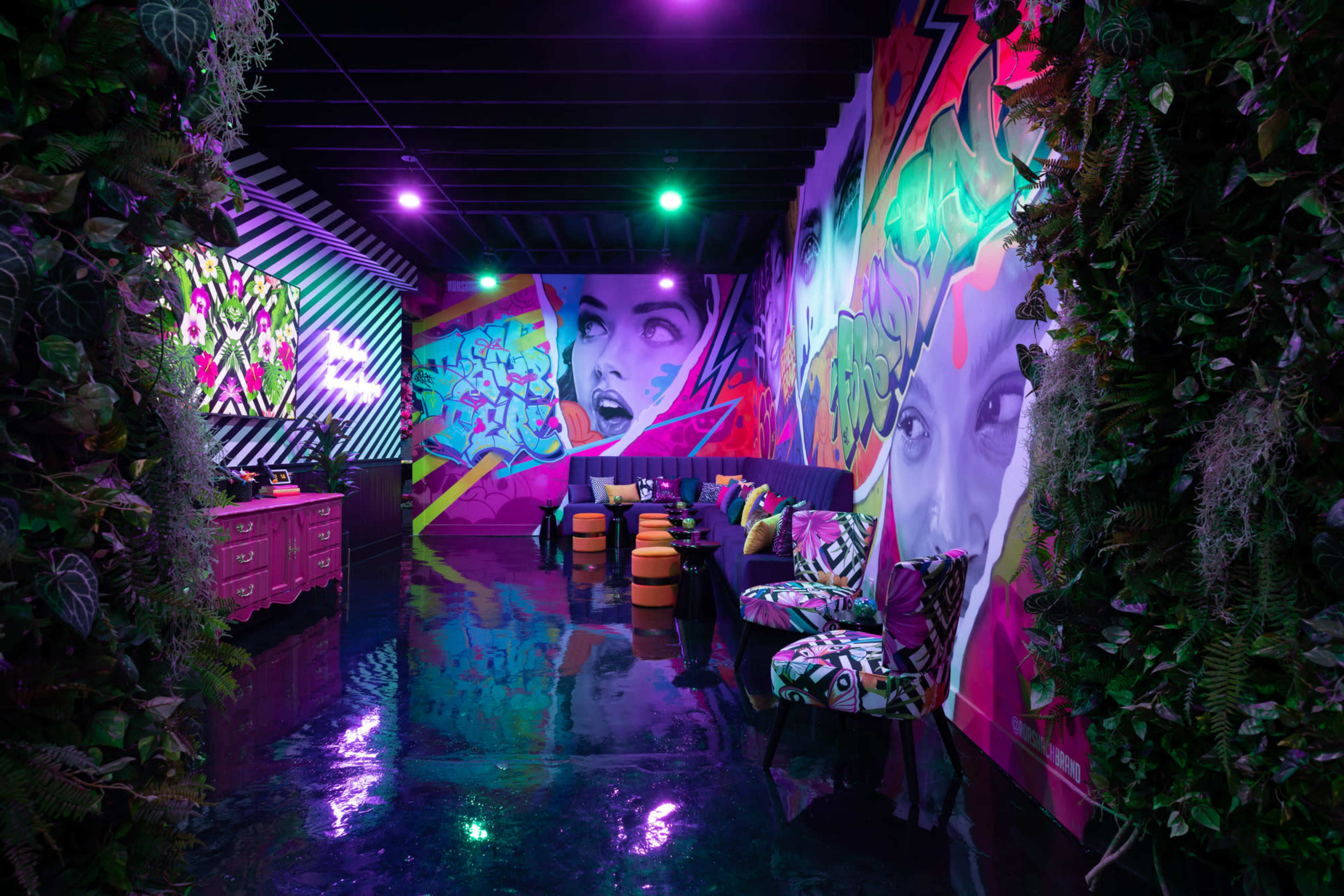 The scene features a brightly colored lounge with vibrant murals on the walls, stylish seating, and a glossy floor reflecting neon lights.