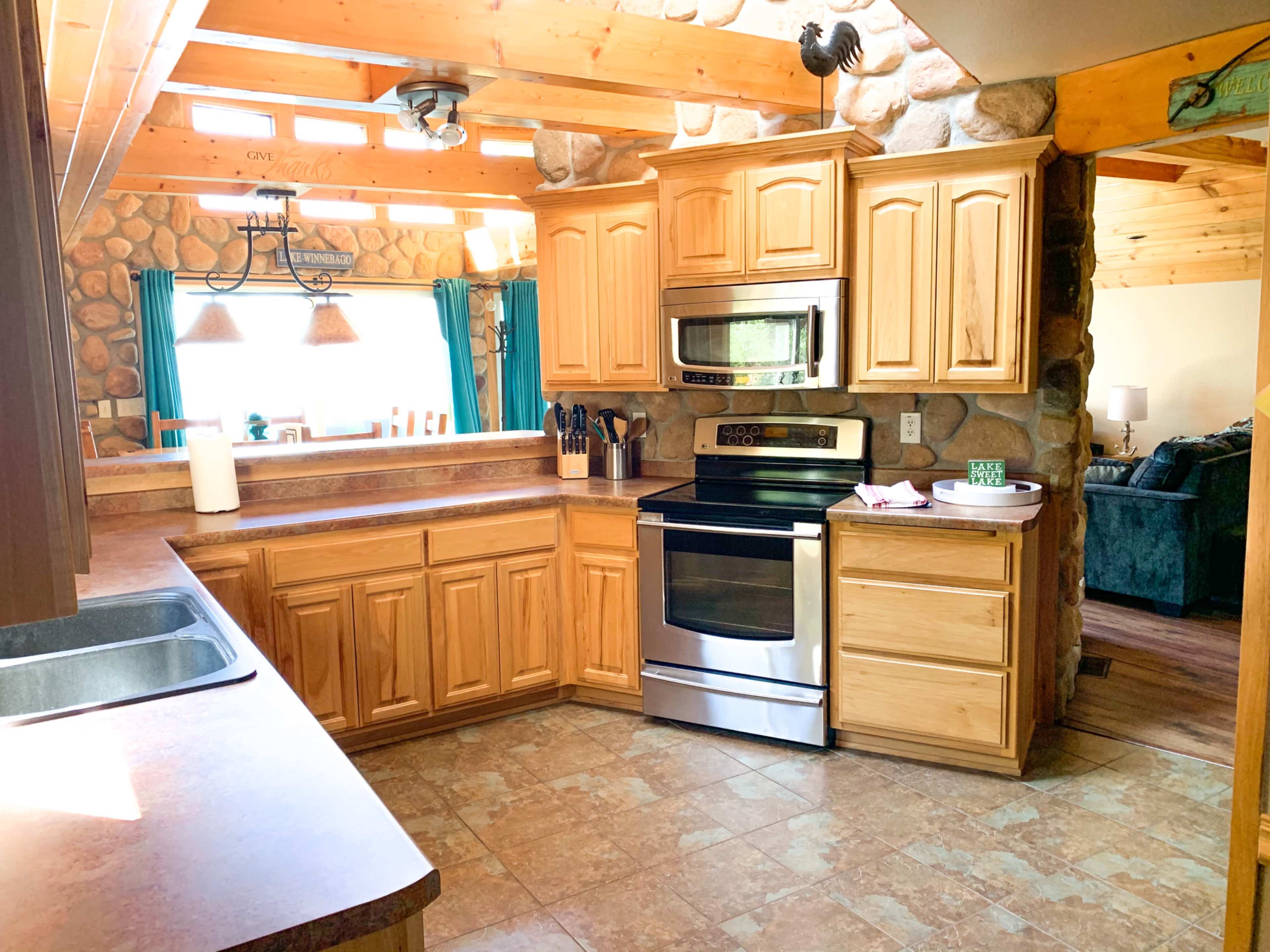 A kitchen with wooden cabinets, a stainless steel stove and microwave, and a stone wall in a rustic setting.