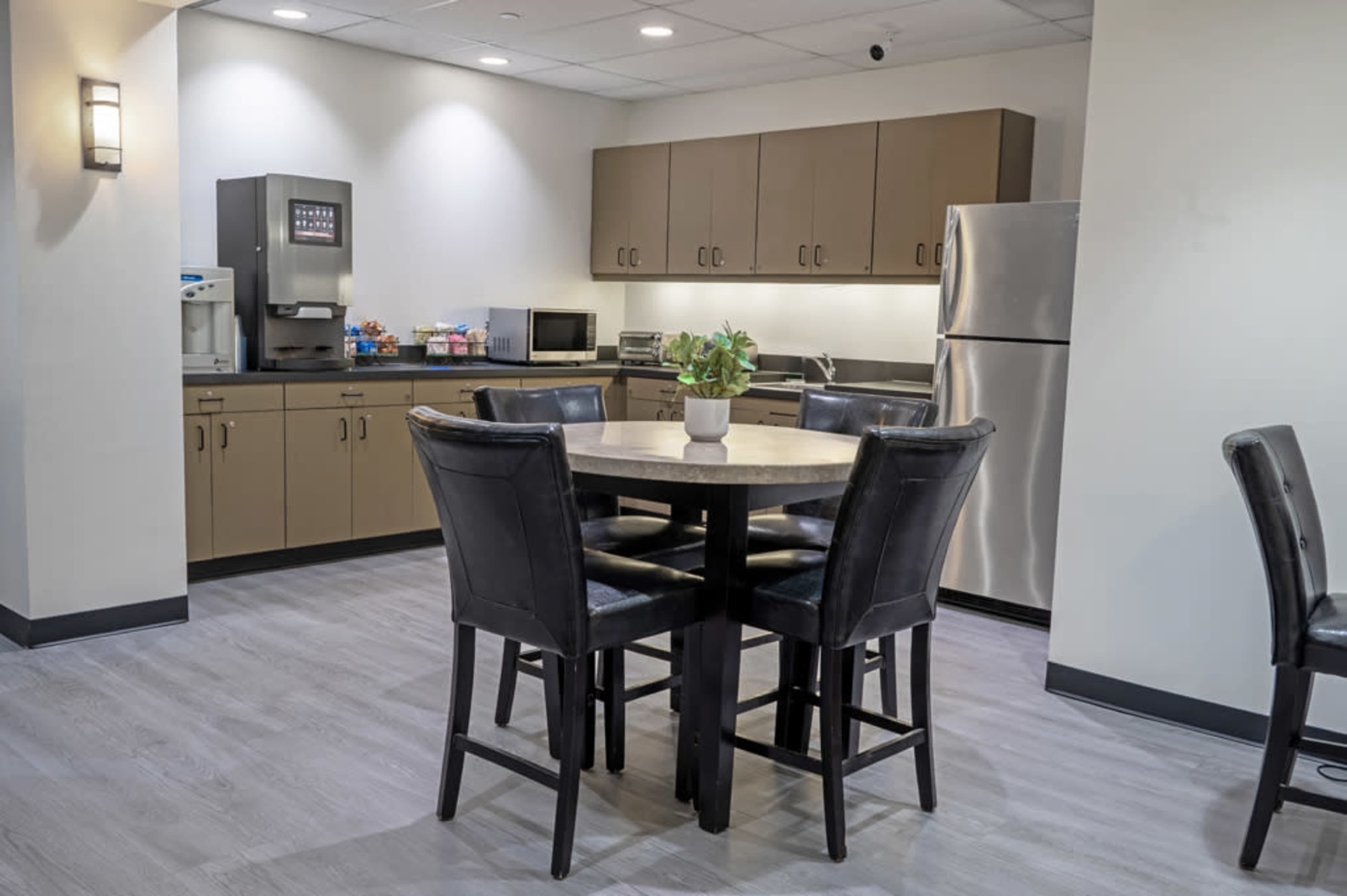 The image shows a kitchen area with a round table surrounded by four chairs, appliances, and cabinets along the walls.