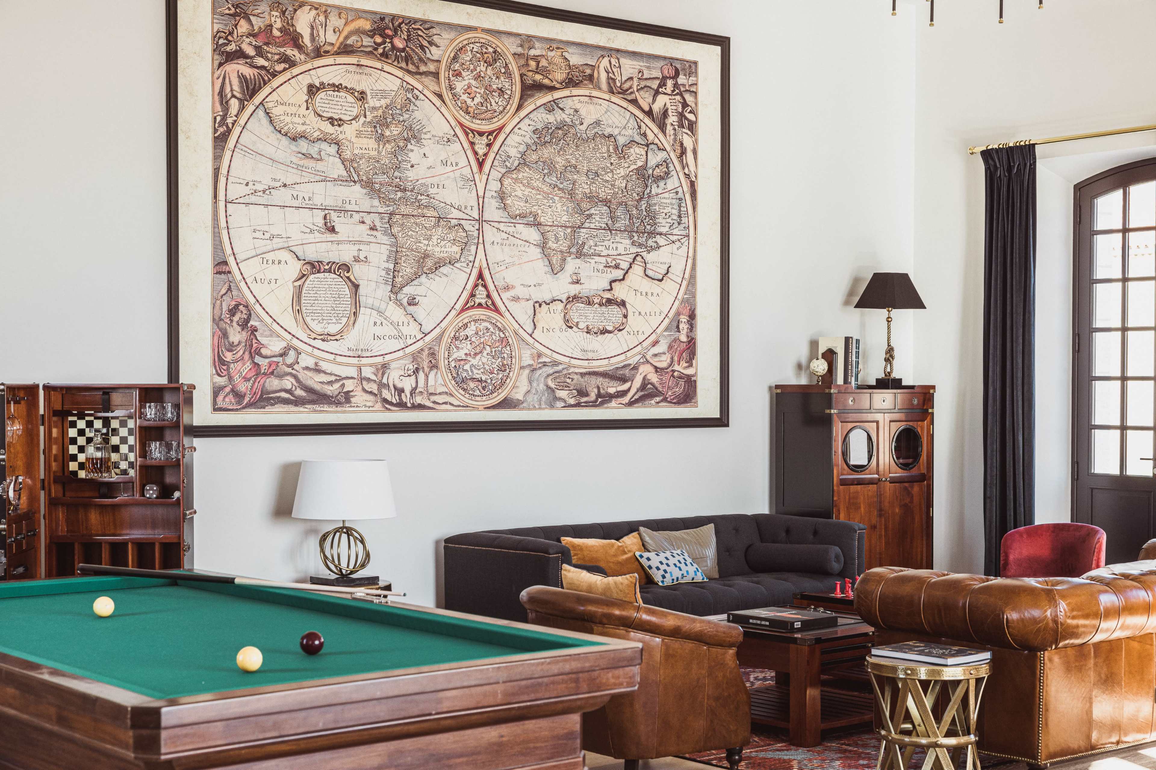 The room features a pool table, a dark sofa, and a large vintage world map framed on the wall.