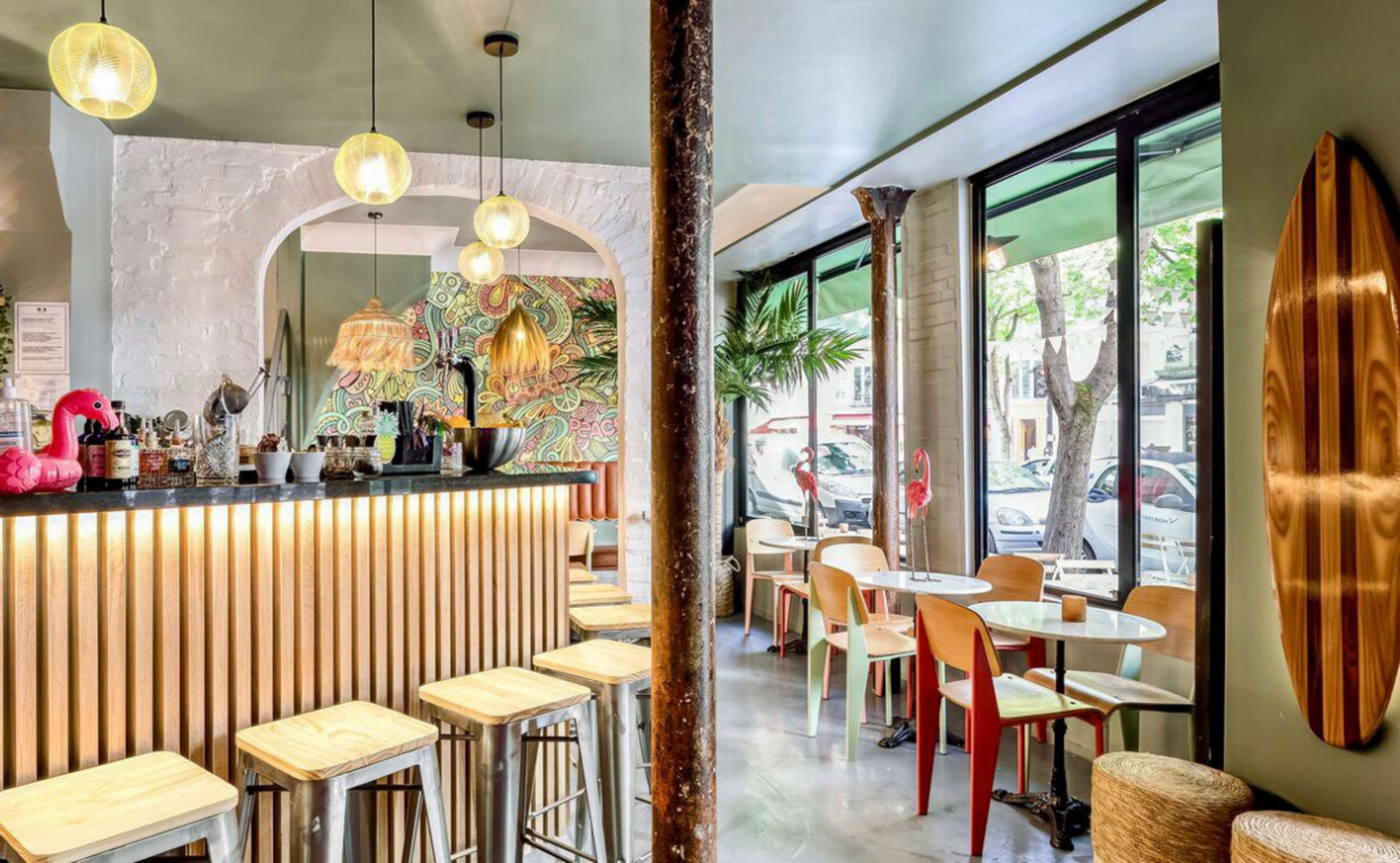 A modern cafe interior featuring a bar with wooden accents, several round tables, and large windows letting in natural light.