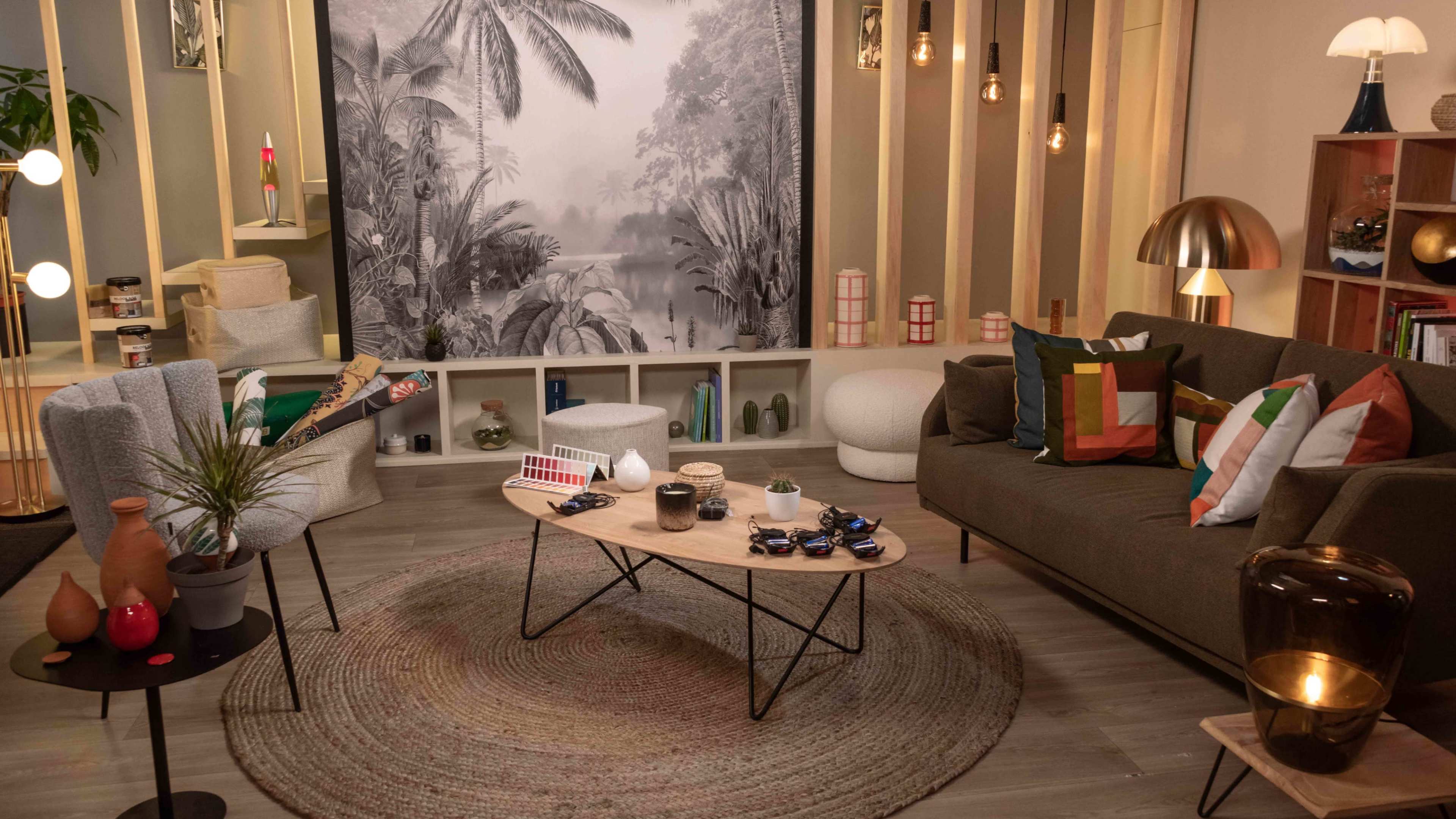 The image depicts a modern living room featuring a circular rug, a wooden coffee table surrounded by two chairs and a sofa, with a large black-and-white mural of a tropical scene on the wall.