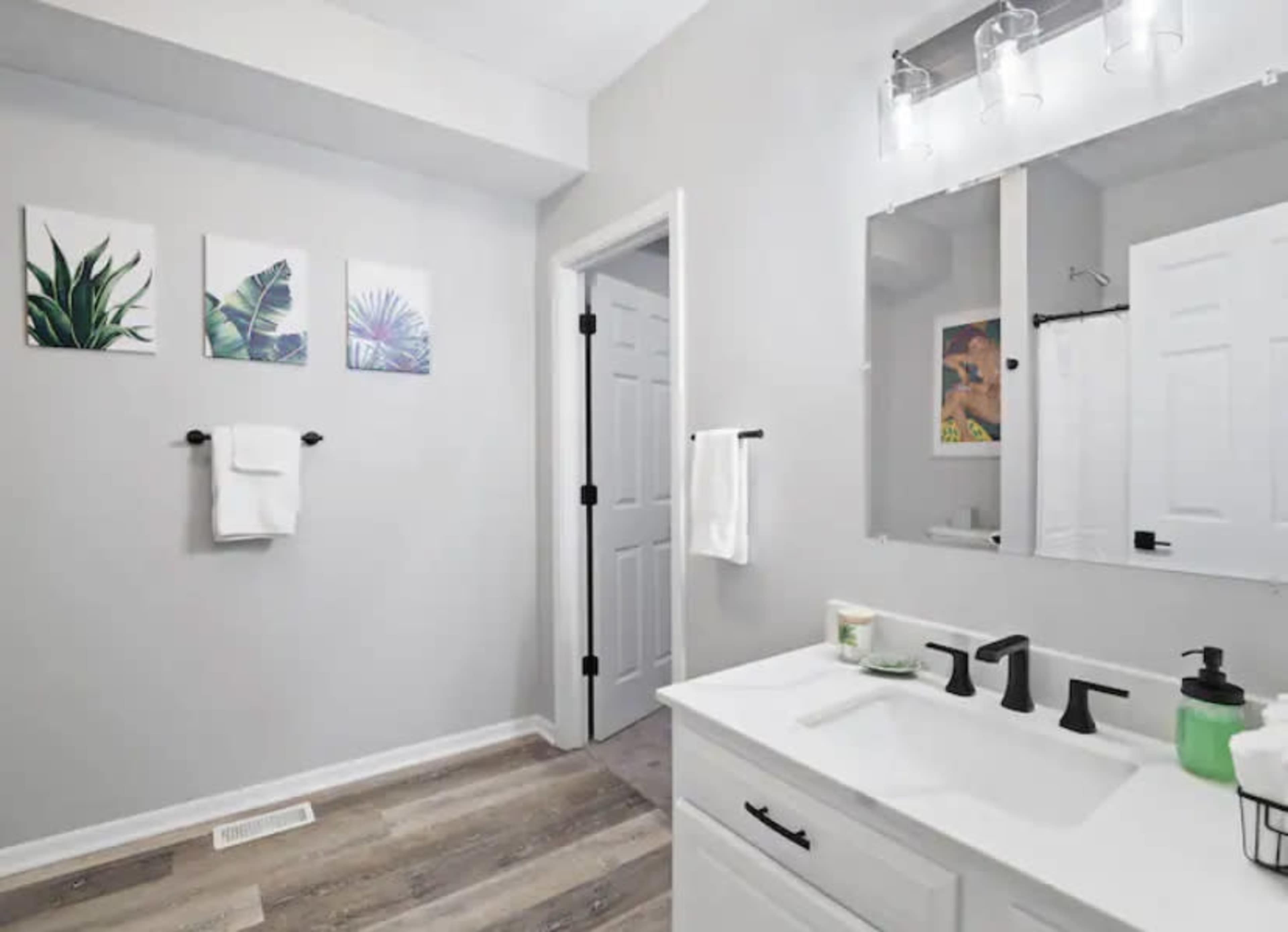 A modern bathroom featuring a white vanity with a sink, gray walls, and tropical plant artwork on the wall.