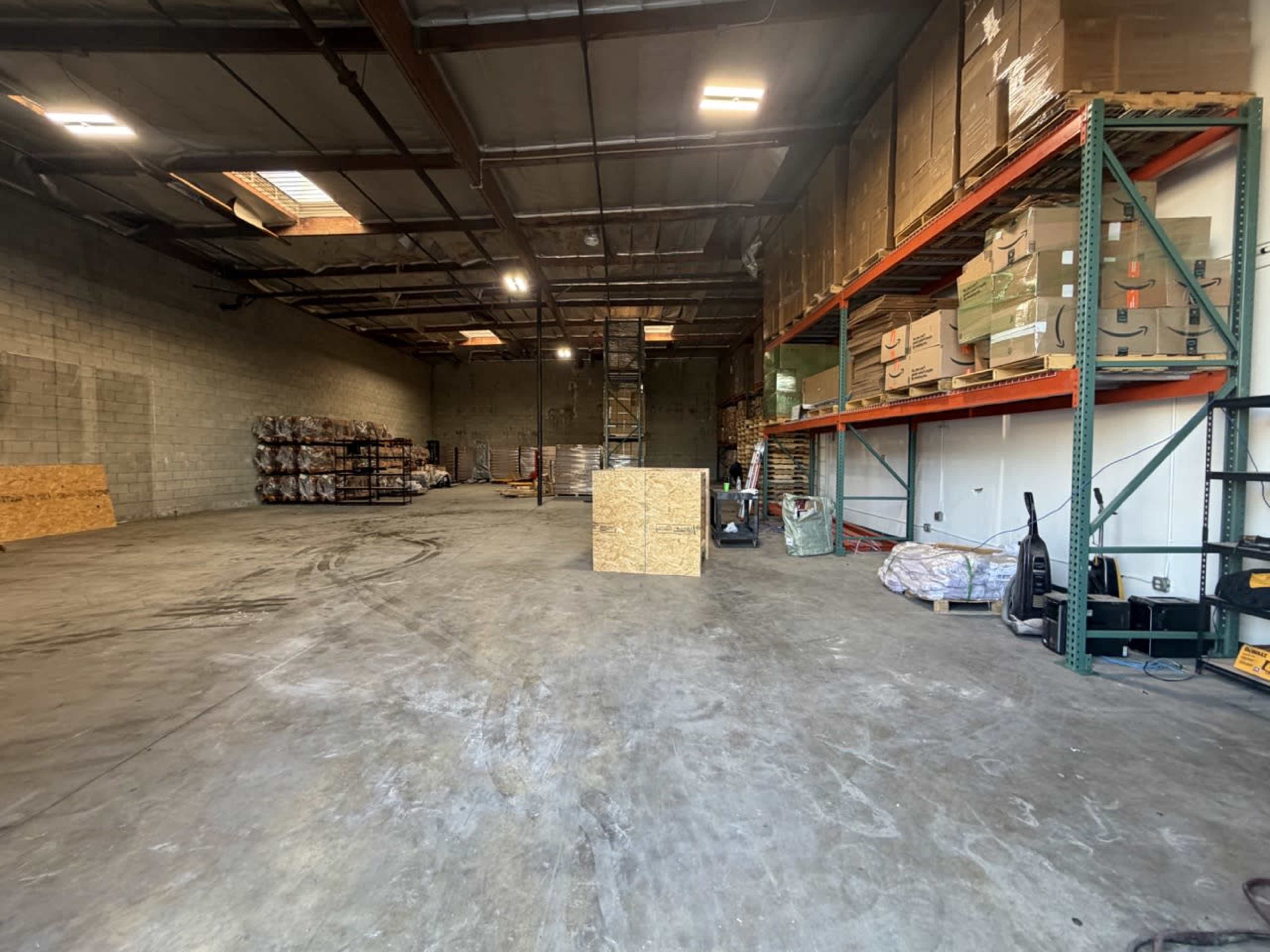 The image shows an empty warehouse space with stacked boxes on shelves and wooden pallets lined against the walls.