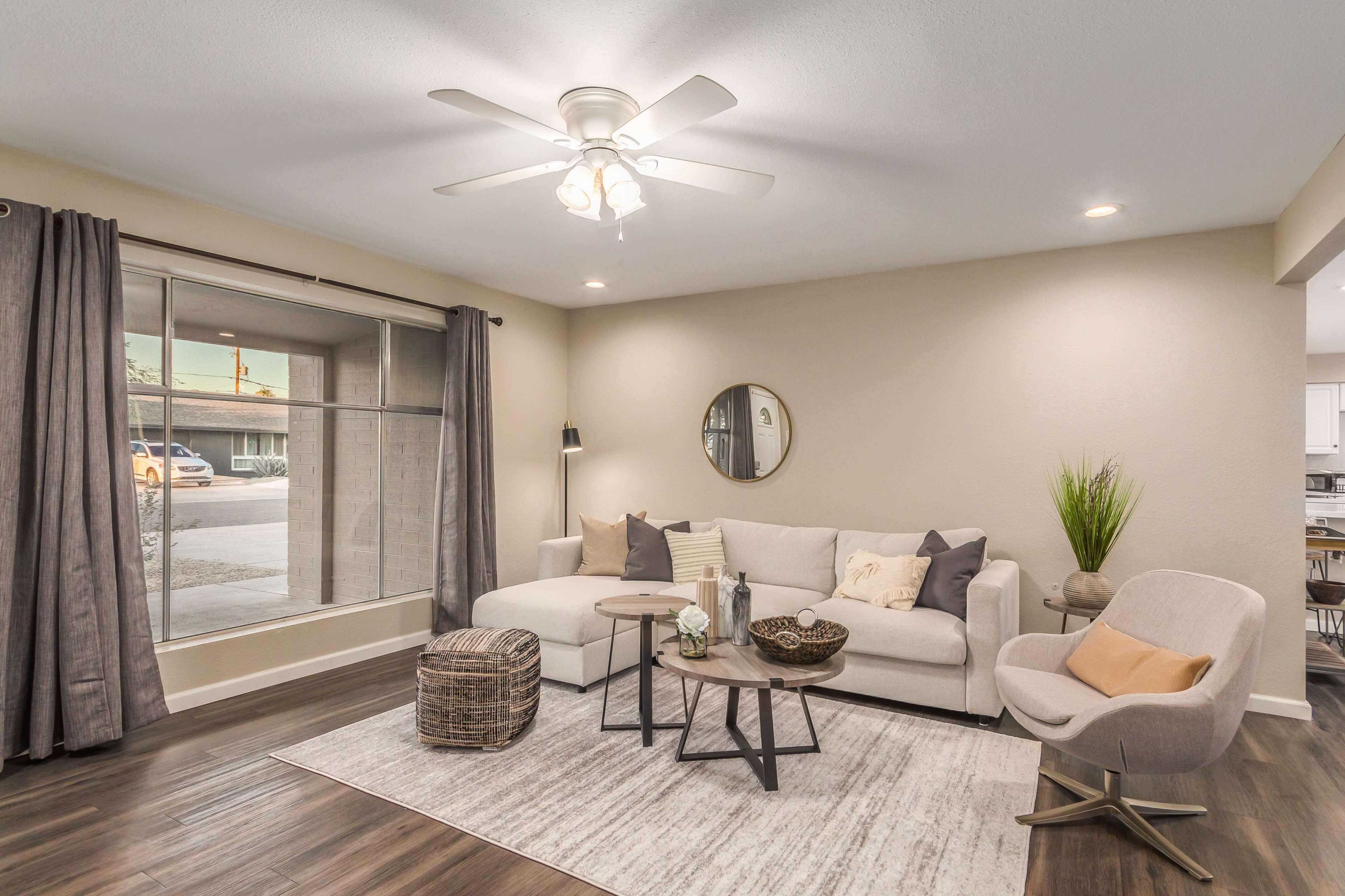A living room features a beige sectional sofa, a round coffee table, and a large window with gray curtains.