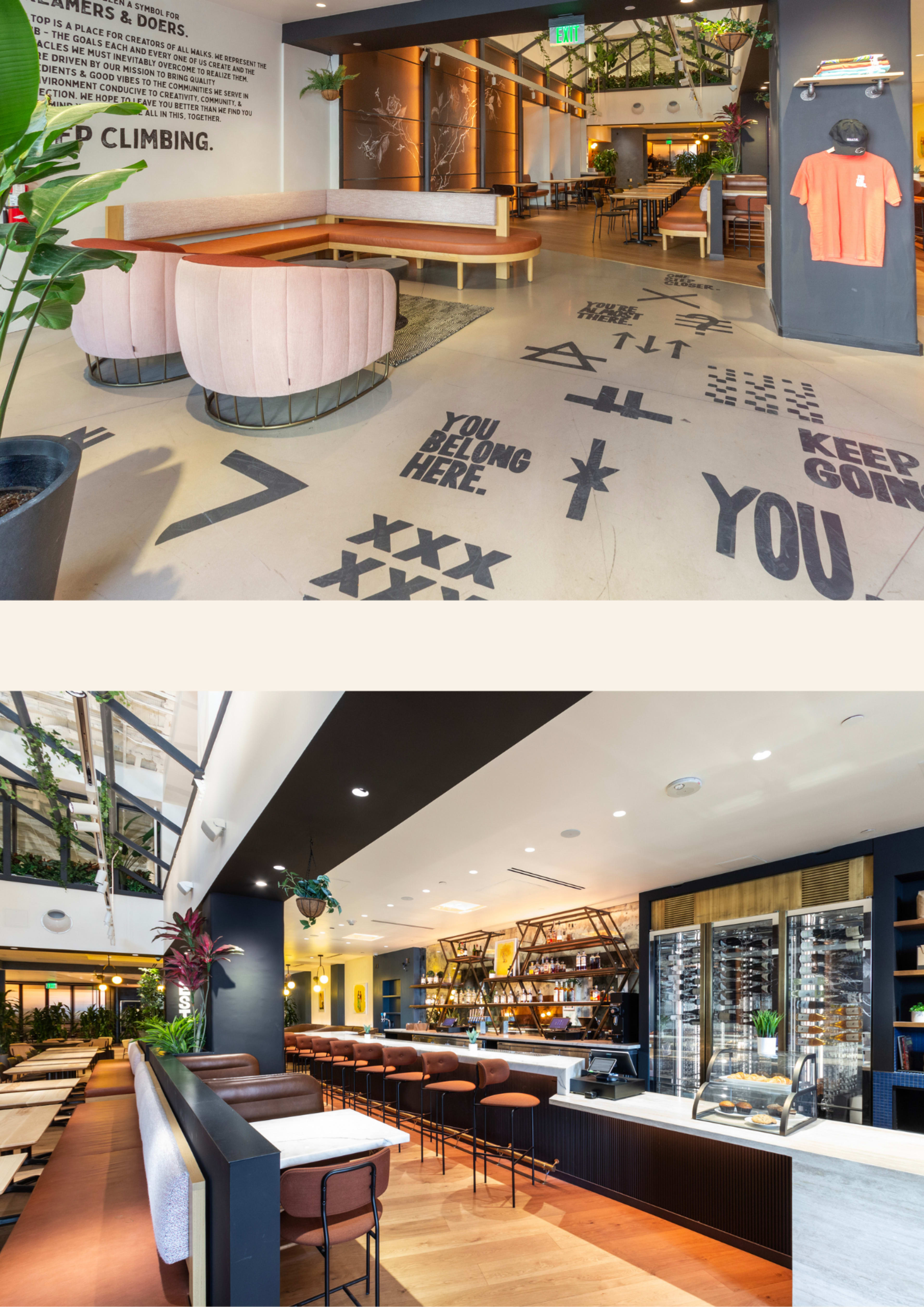 The image shows a modern indoor space featuring a seating area with pink lounge chairs and a café/bar setup with shelves of drinks and a wooden counter, surrounded by greenery and decorative wall text.