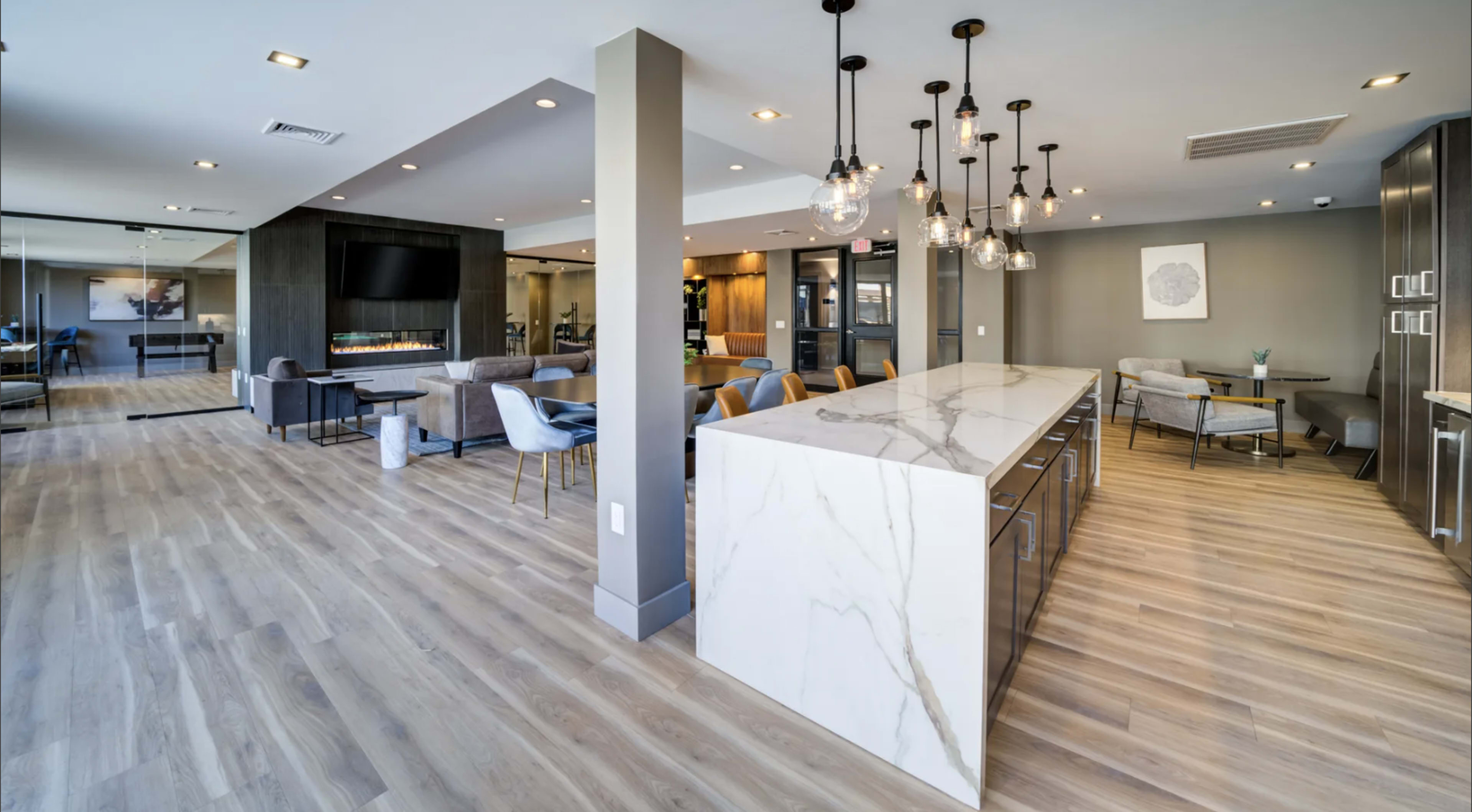 The image shows a modern, open-concept living space with a large kitchen island, stylish seating areas, and contemporary lighting fixtures.