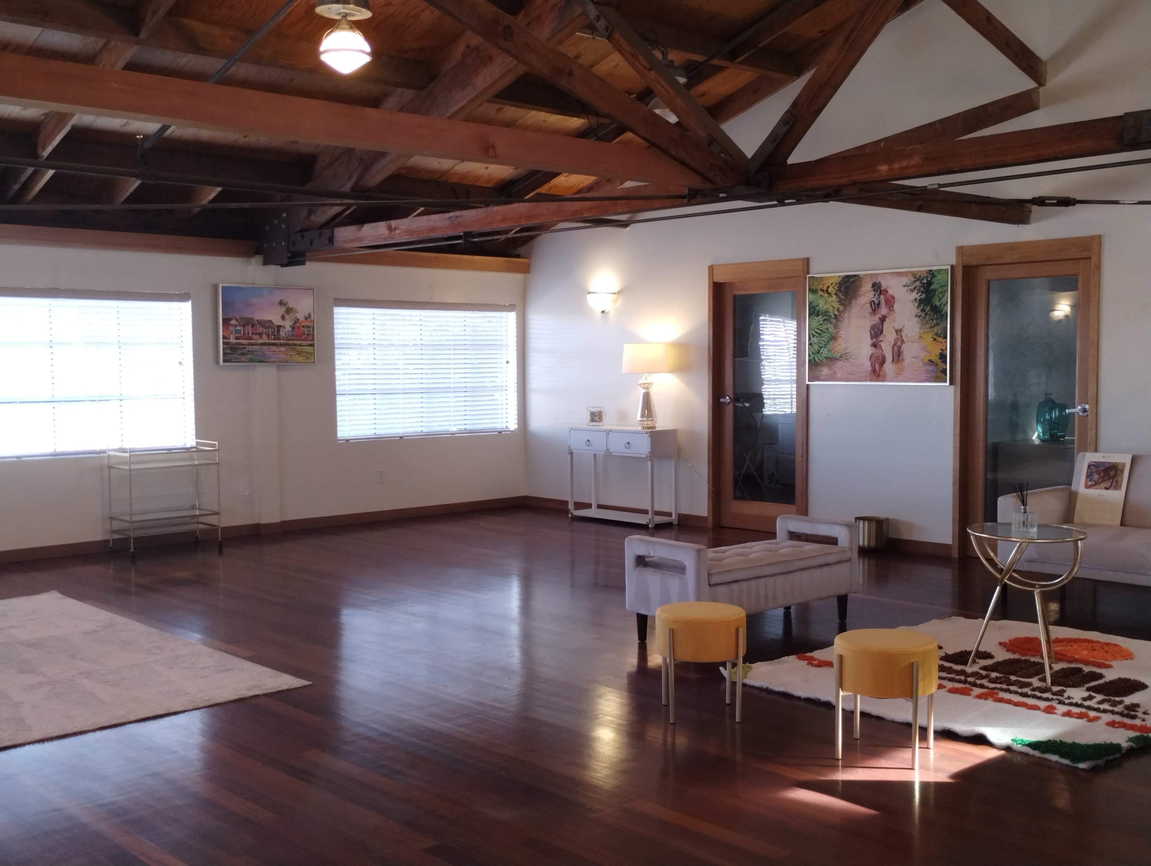 A spacious room with wooden beams, hardwood flooring, and a seating arrangement that includes a small table and chairs, along with decorative artwork on the walls.