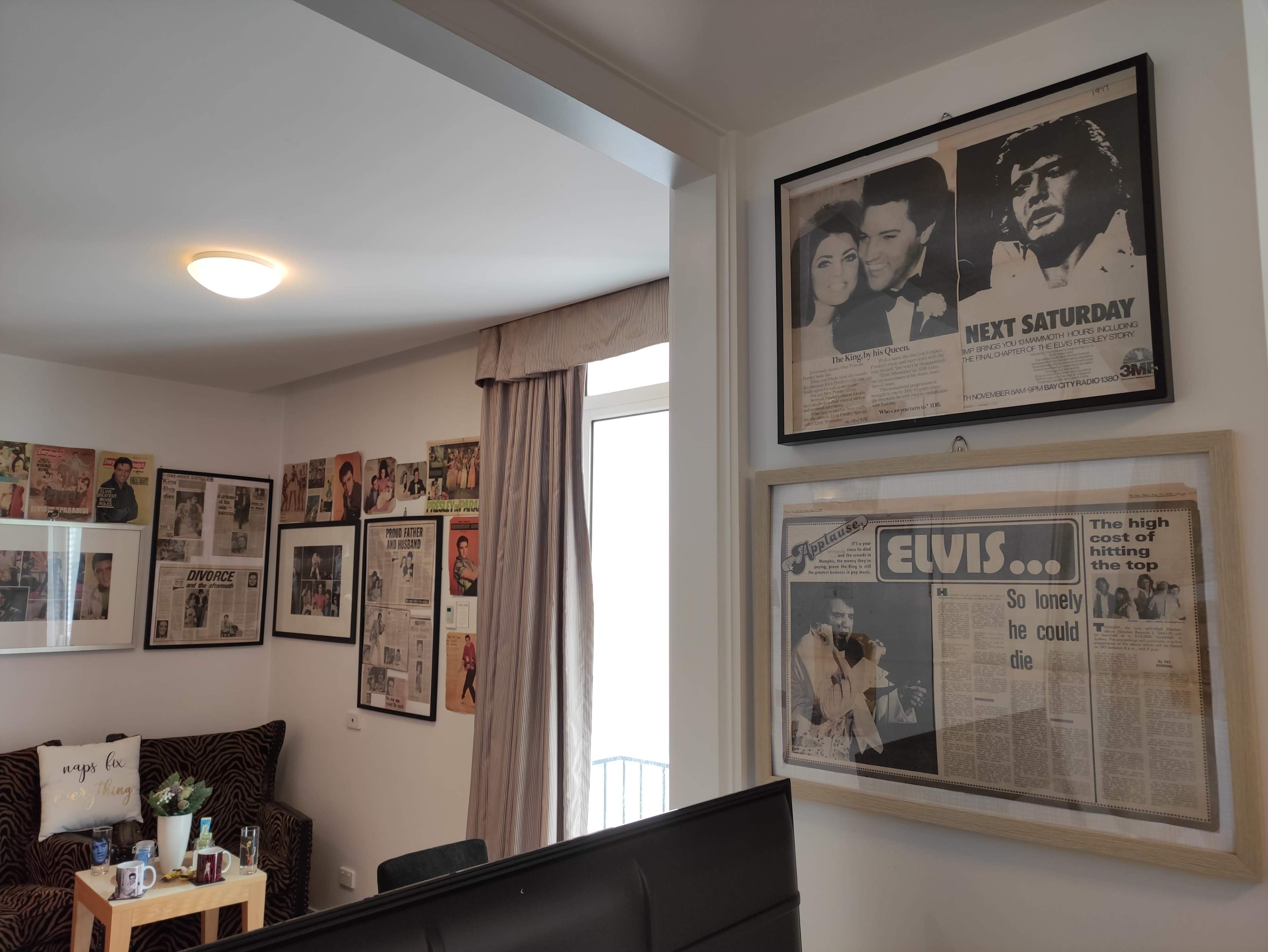 A living room with framed newspaper clippings and photographs of Elvis Presley displayed on the walls, along with a cozy seating area and a coffee table.