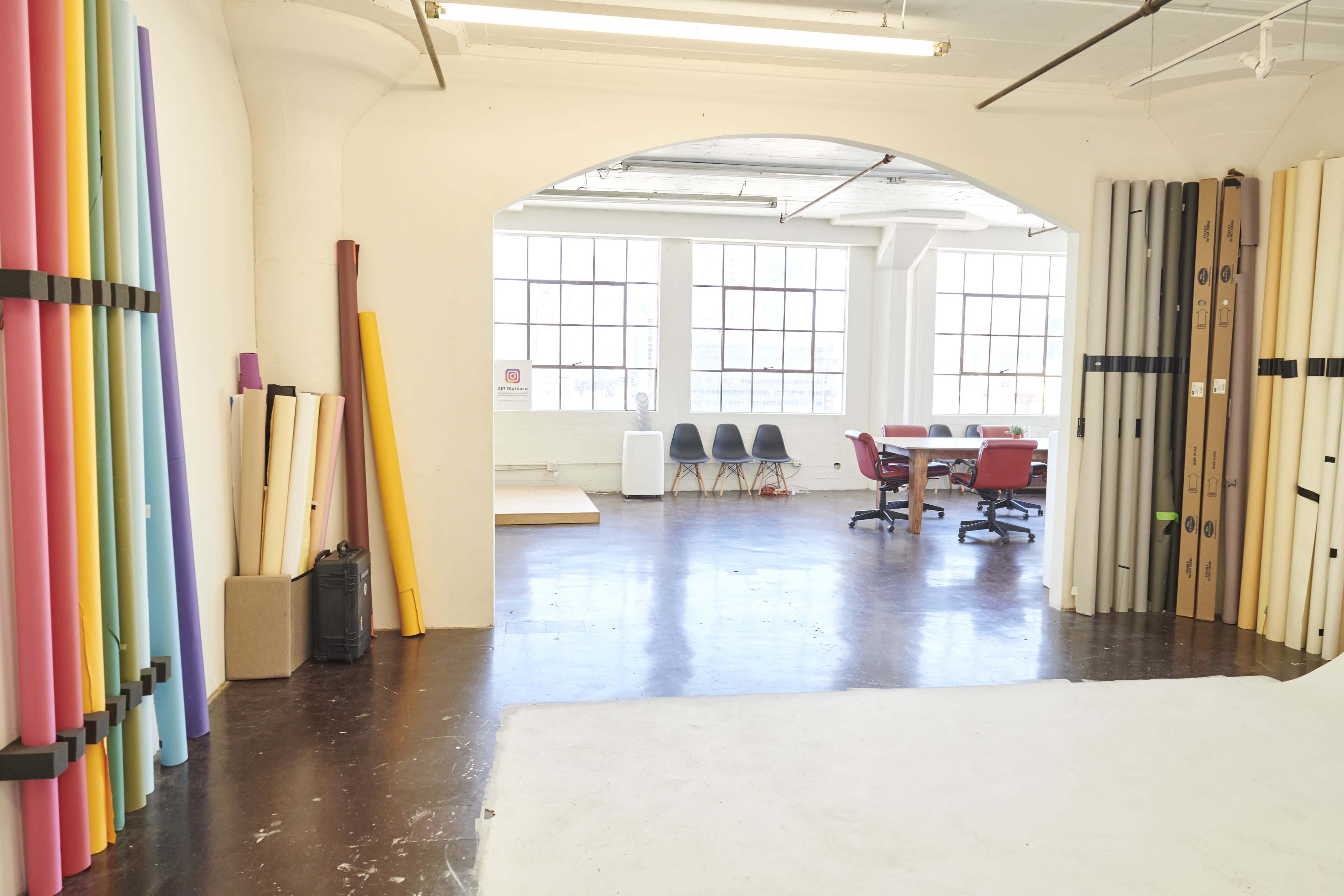 A spacious studio filled with colorful backdrops on the left and a table with chairs in the center against large windows that allow natural light to fill the room.