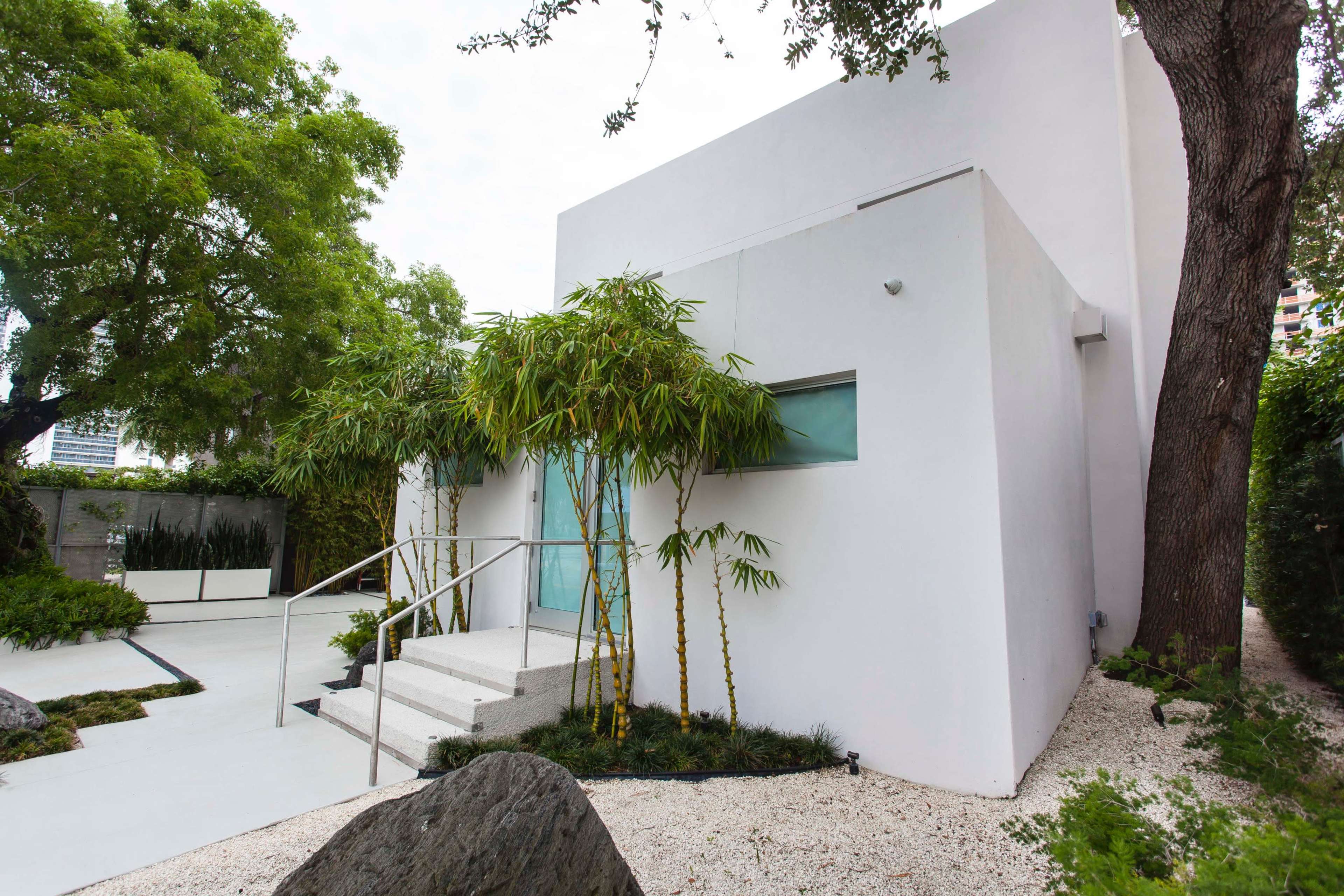 A modern white building with large windows is surrounded by greenery and decorative rocks.